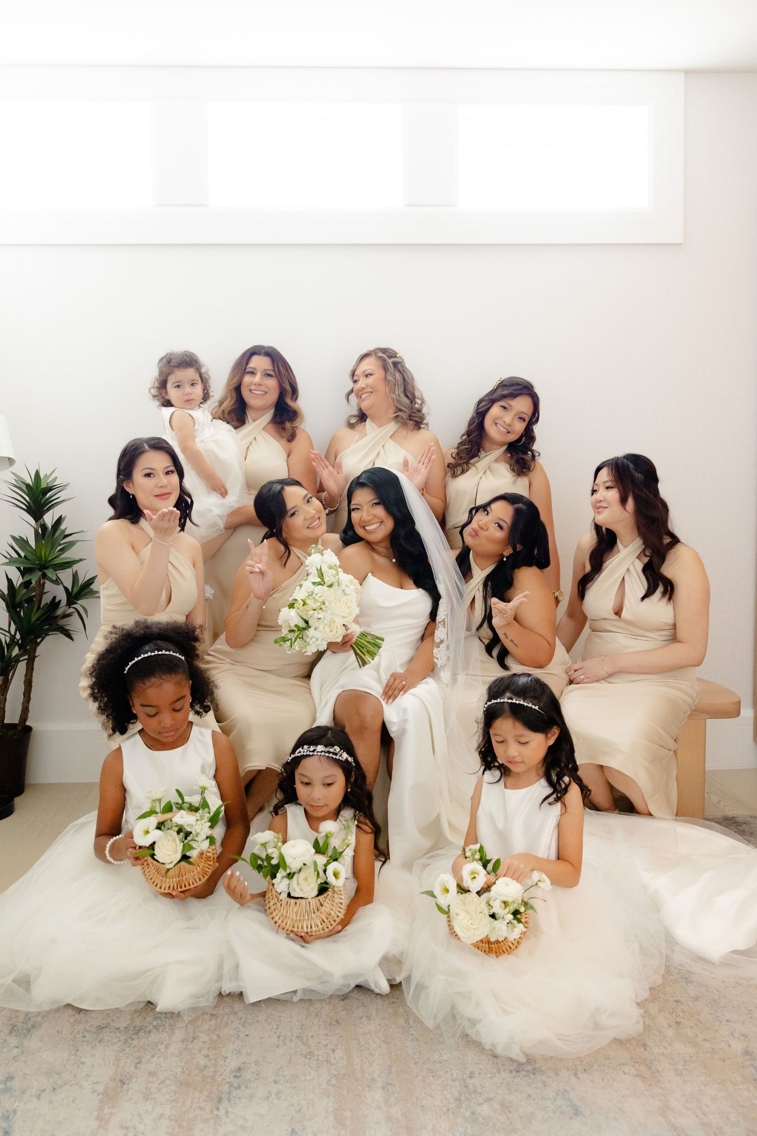Wedding party with flower girls pose together in cream and white dresses holding bouquets.