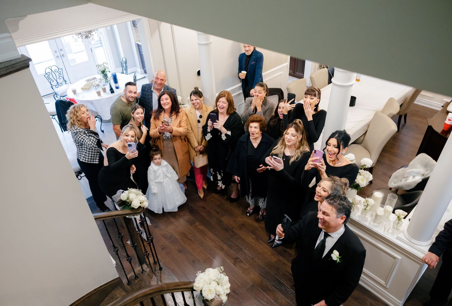 Wedding party cheers from staircase as newlyweds celebrate below.