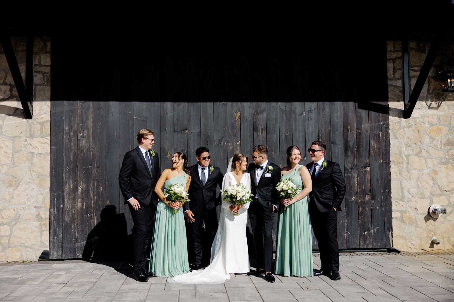 Wedding party poses against wooden barn door with bridesmaids wearing seafoam green dresses.