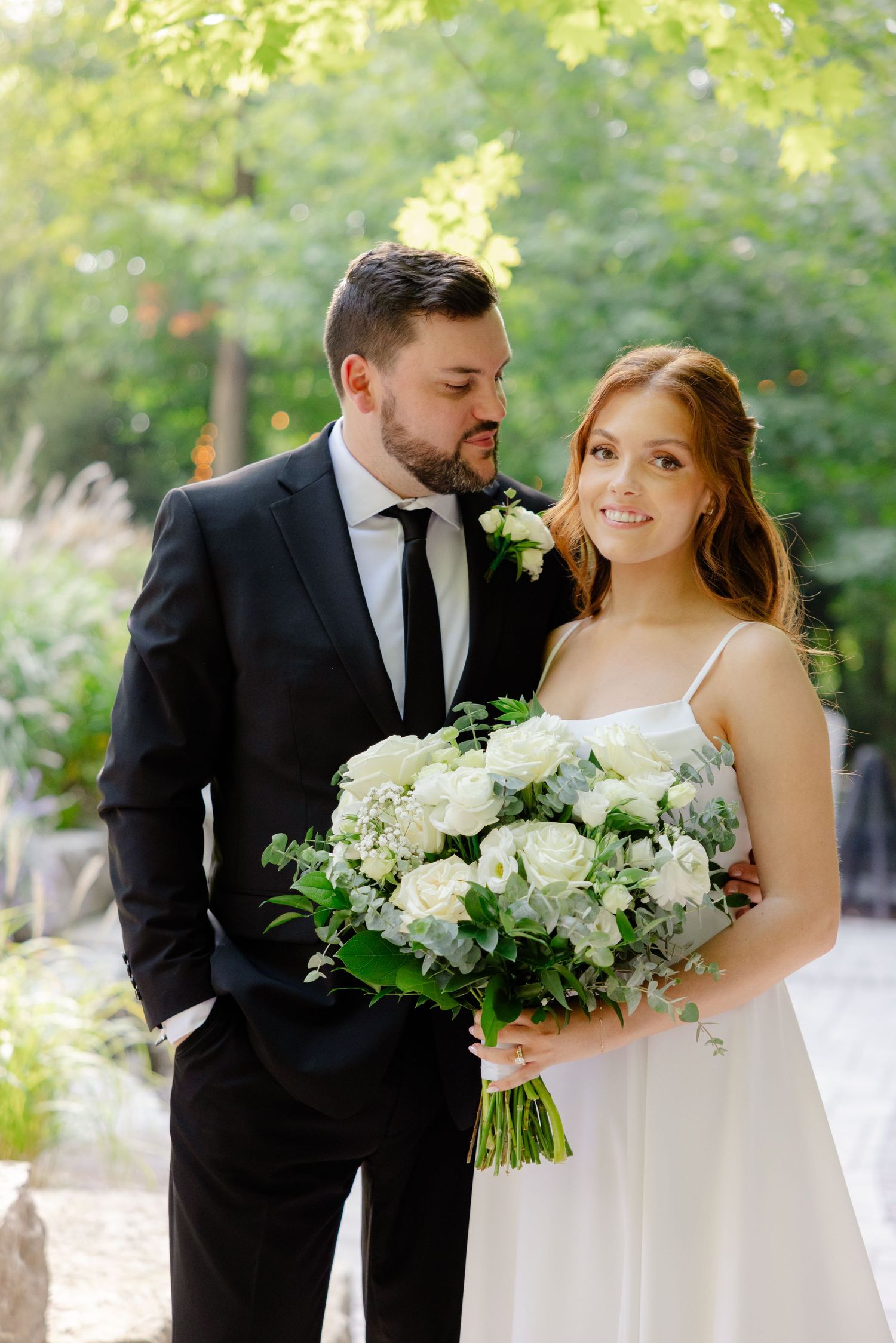Intimate wedding portrait outdoors with lush greenery and white floral bouquet.