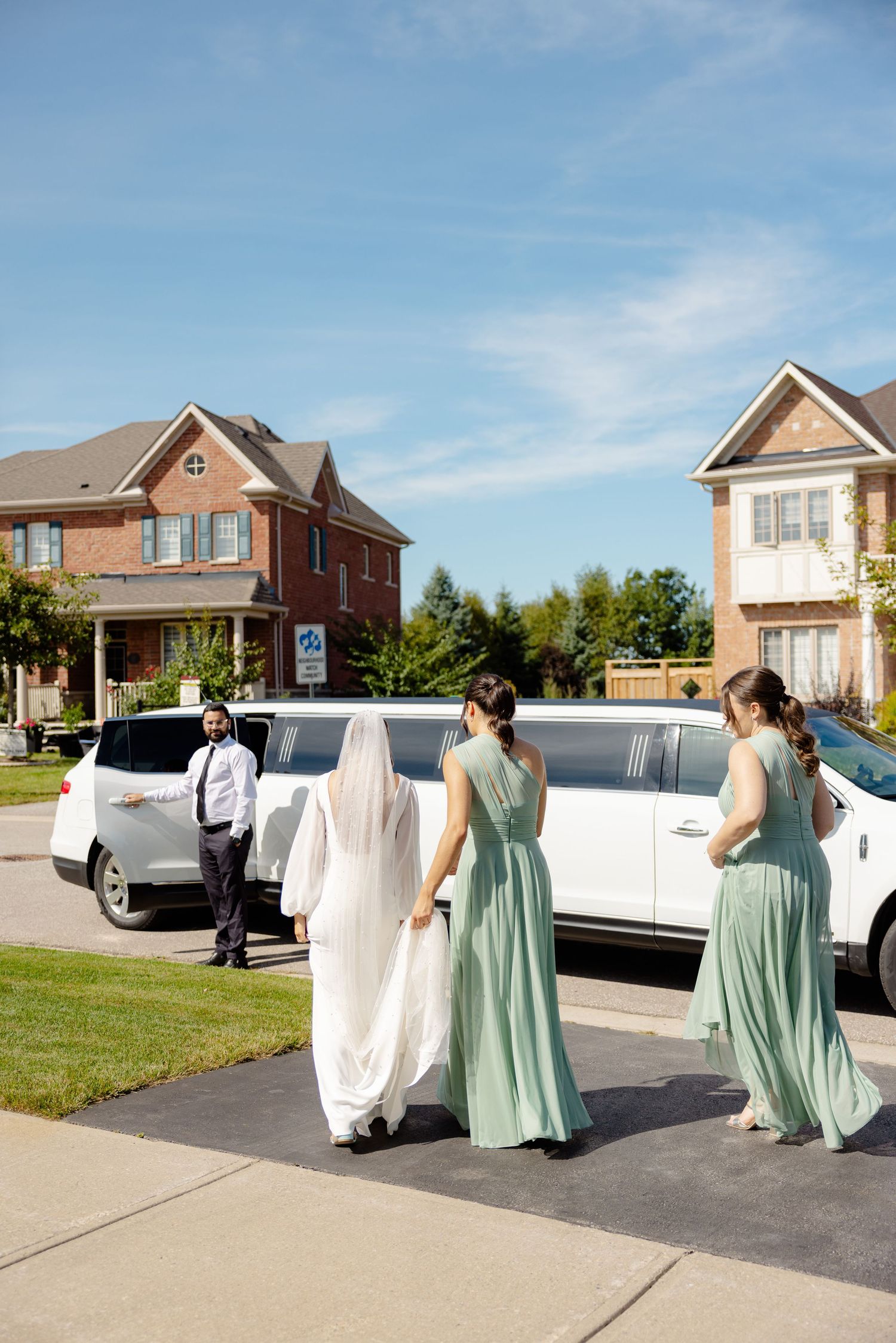 Wedding party in mint green and white dresses walking toward a white limousine.