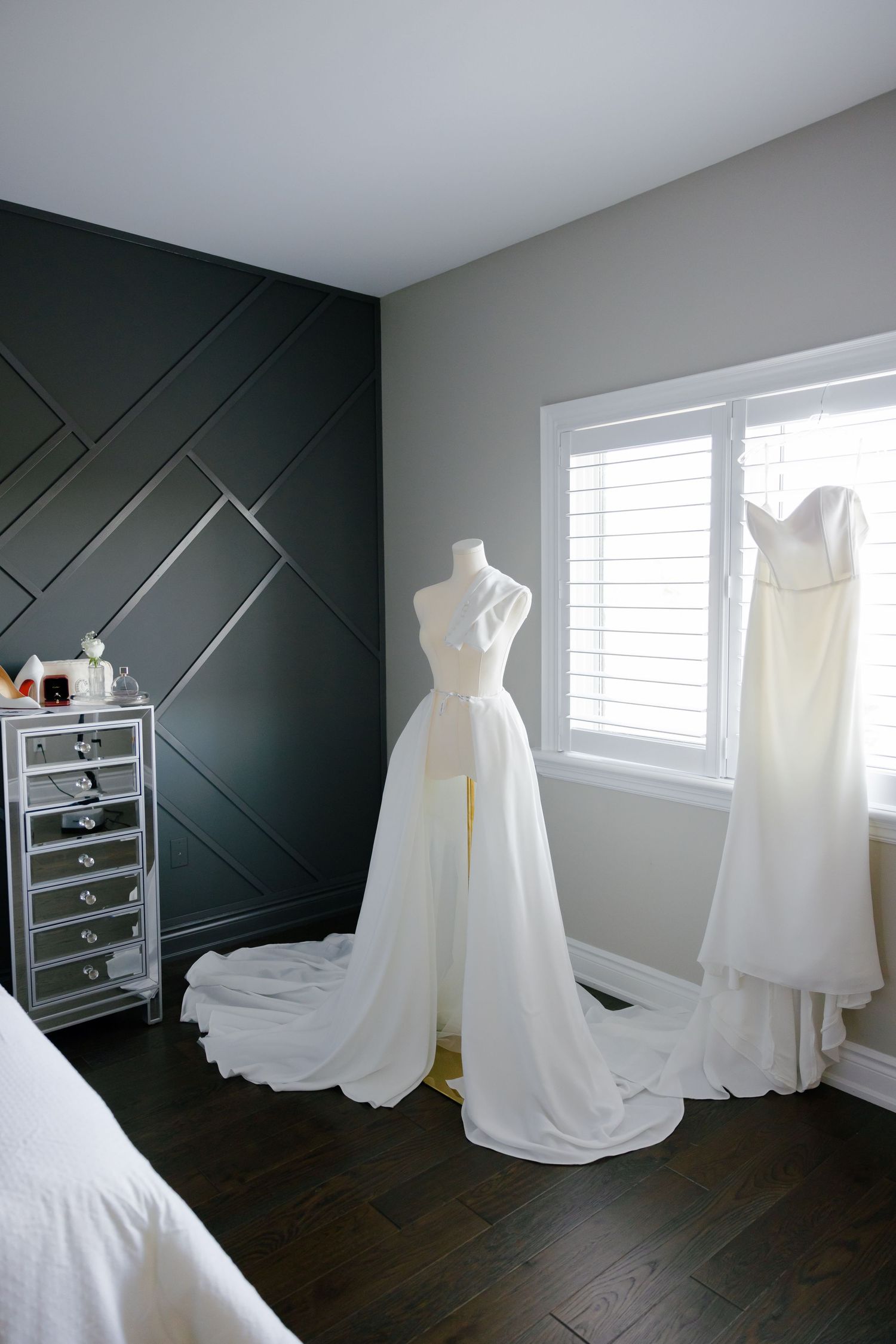 Elegant white wedding dresses displayed in a room with dark geometric wall paneling.