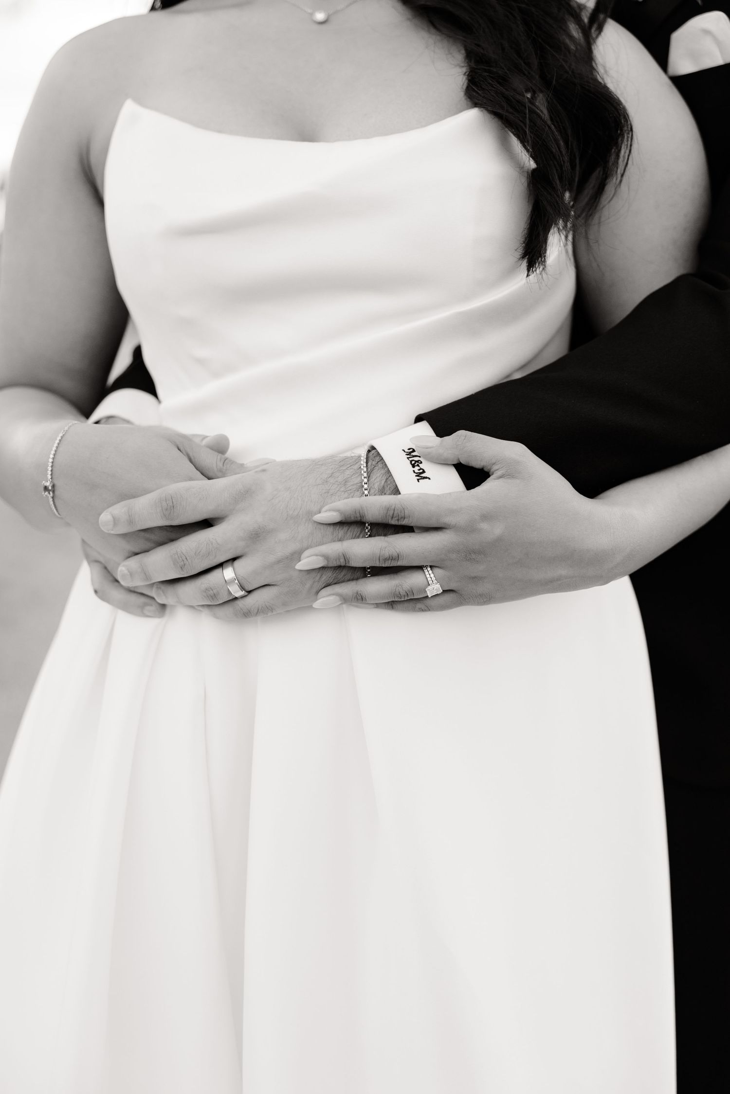Black and white detail shot of hands with wedding rings against elegant bridal gown.