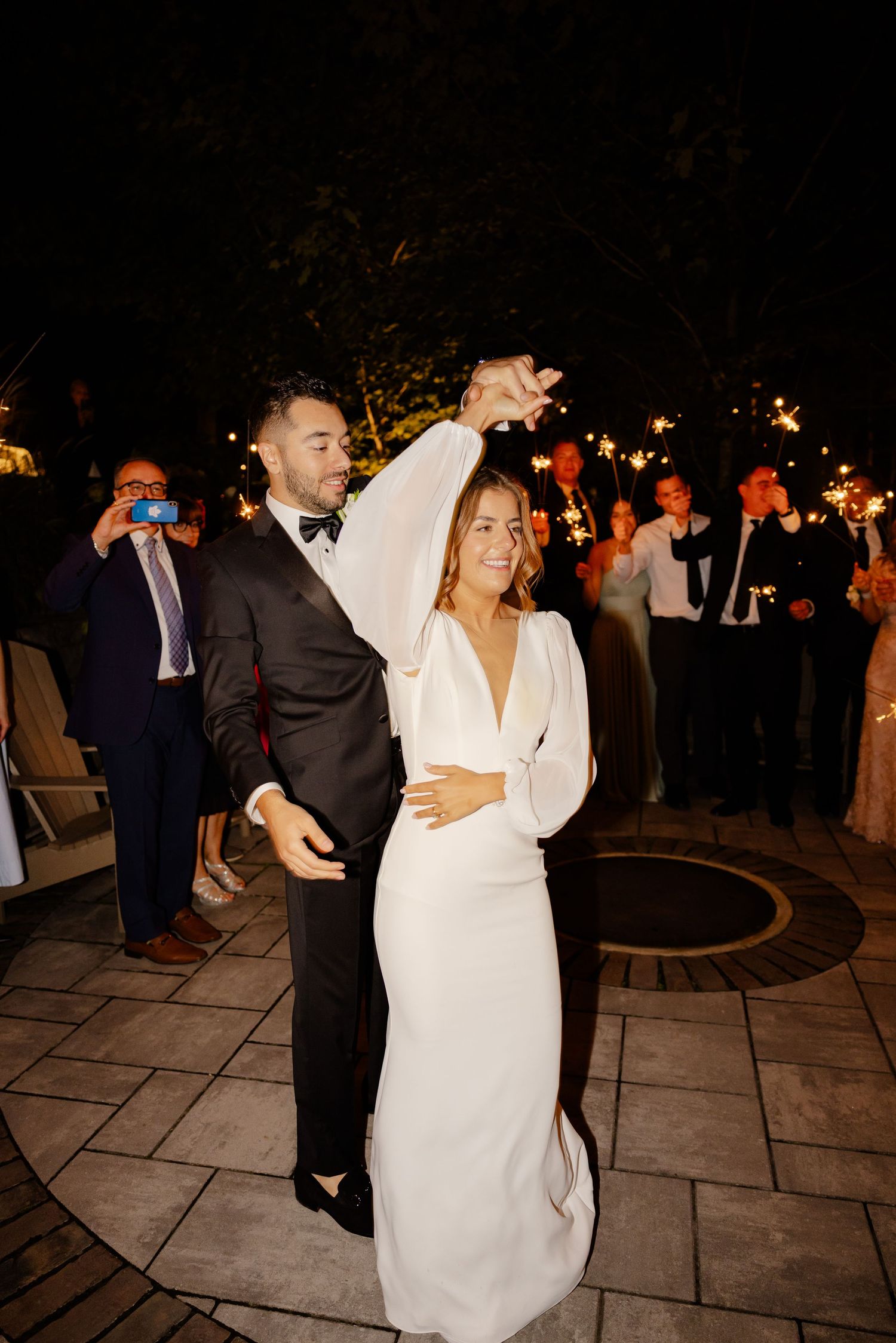 A couple dances together at their nighttime wedding reception on a stone patio.