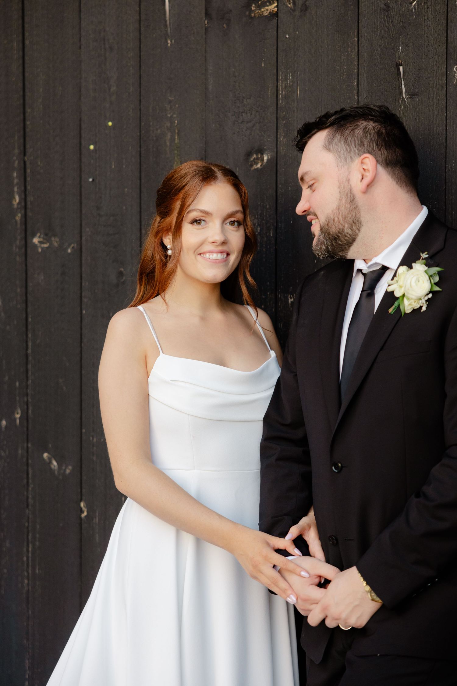 Intimate wedding portrait with couple sharing joyful moment against wooden backdrop.