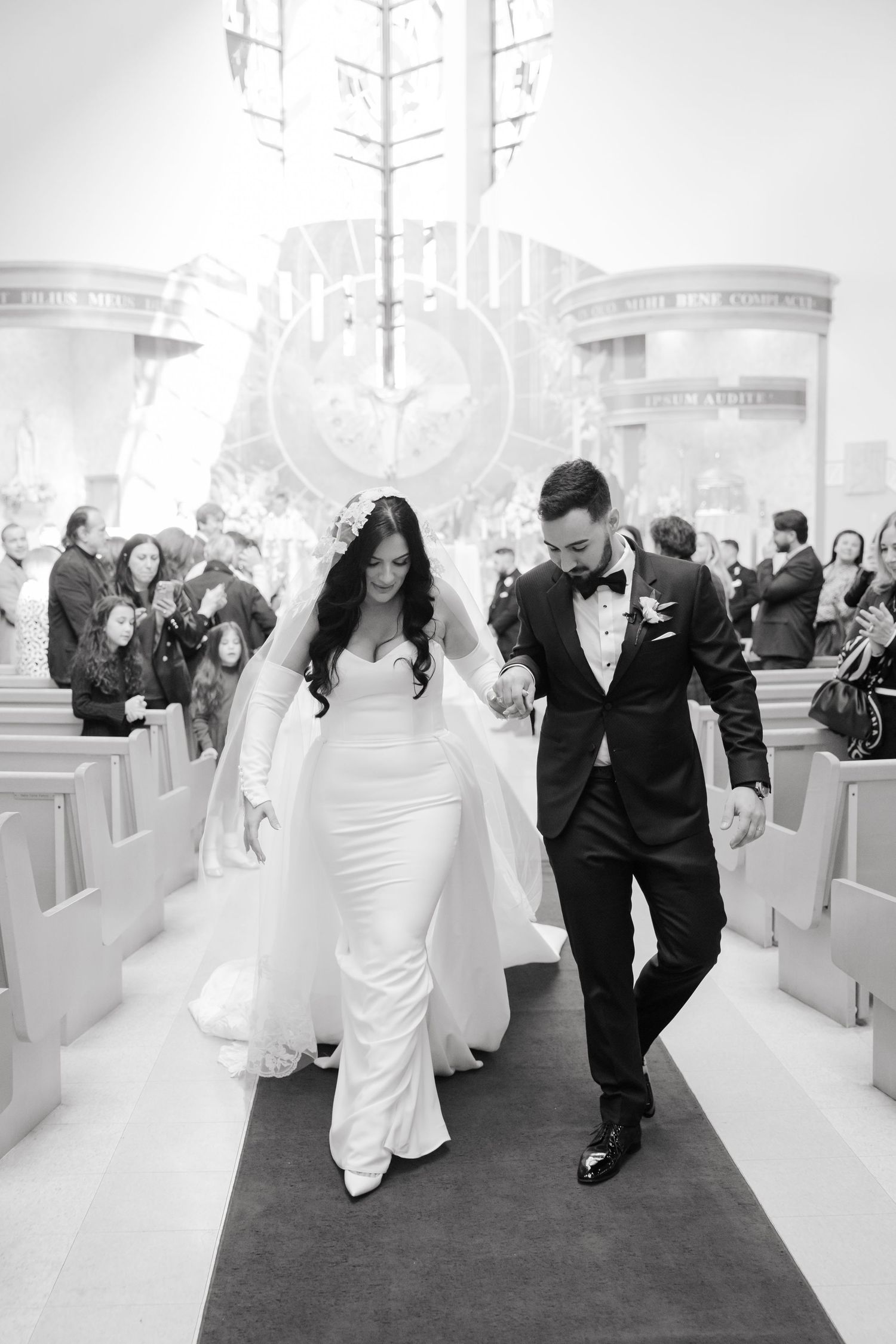 A bride and groom walk down the aisle of a church after their ceremony in this black and white wedding photo.