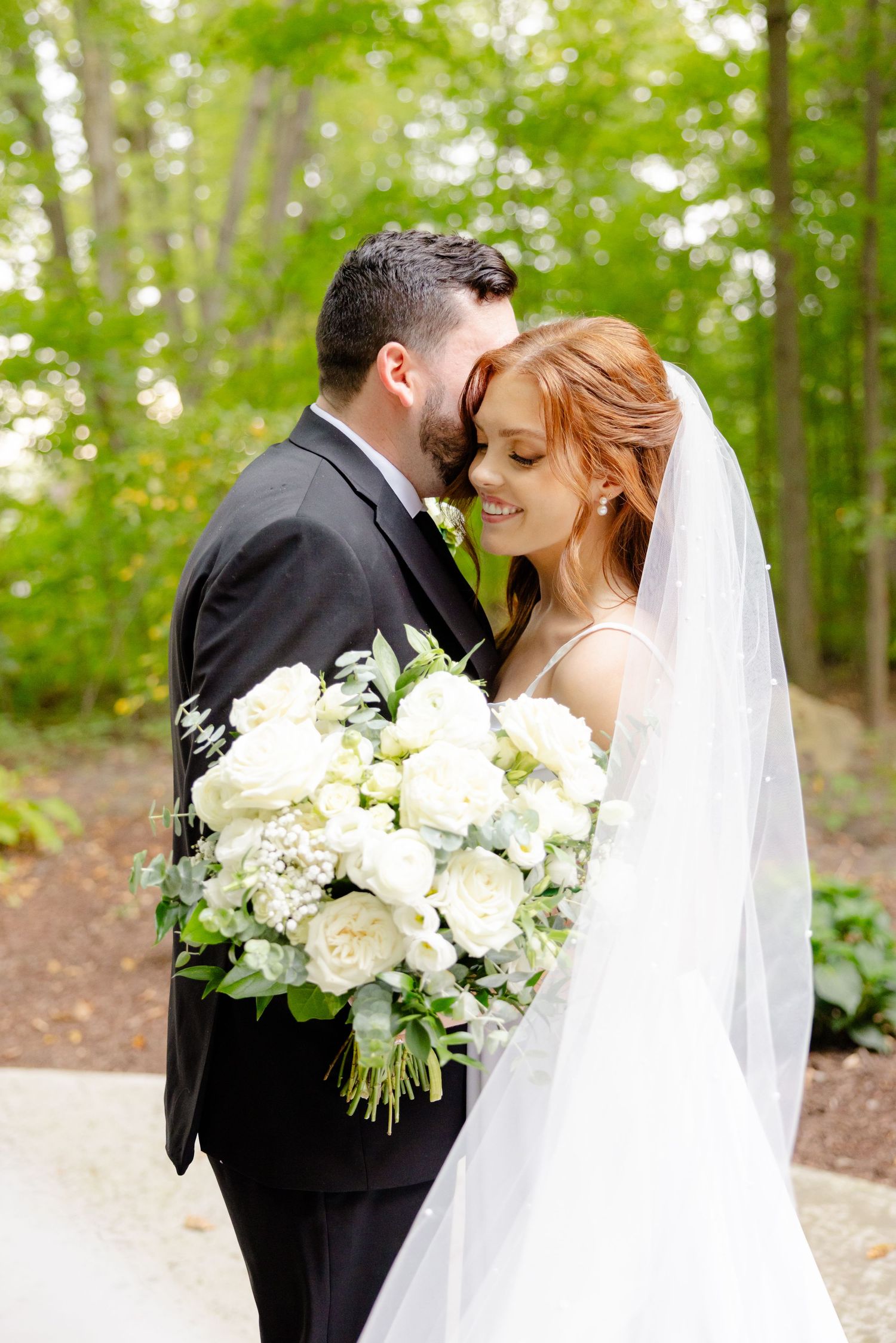 An intimate wedding portrait with white florals and flowing veil in a lush garden setting.
