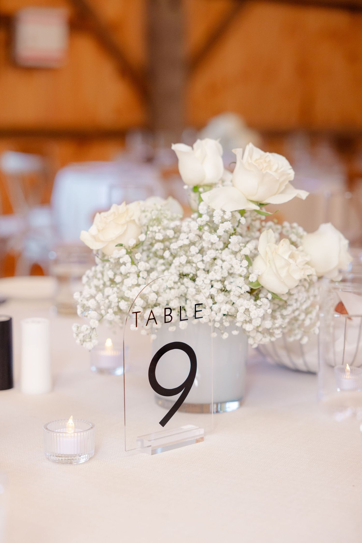 Table centerpiece with white roses and baby's breath in frosted vase next to table number nine.
