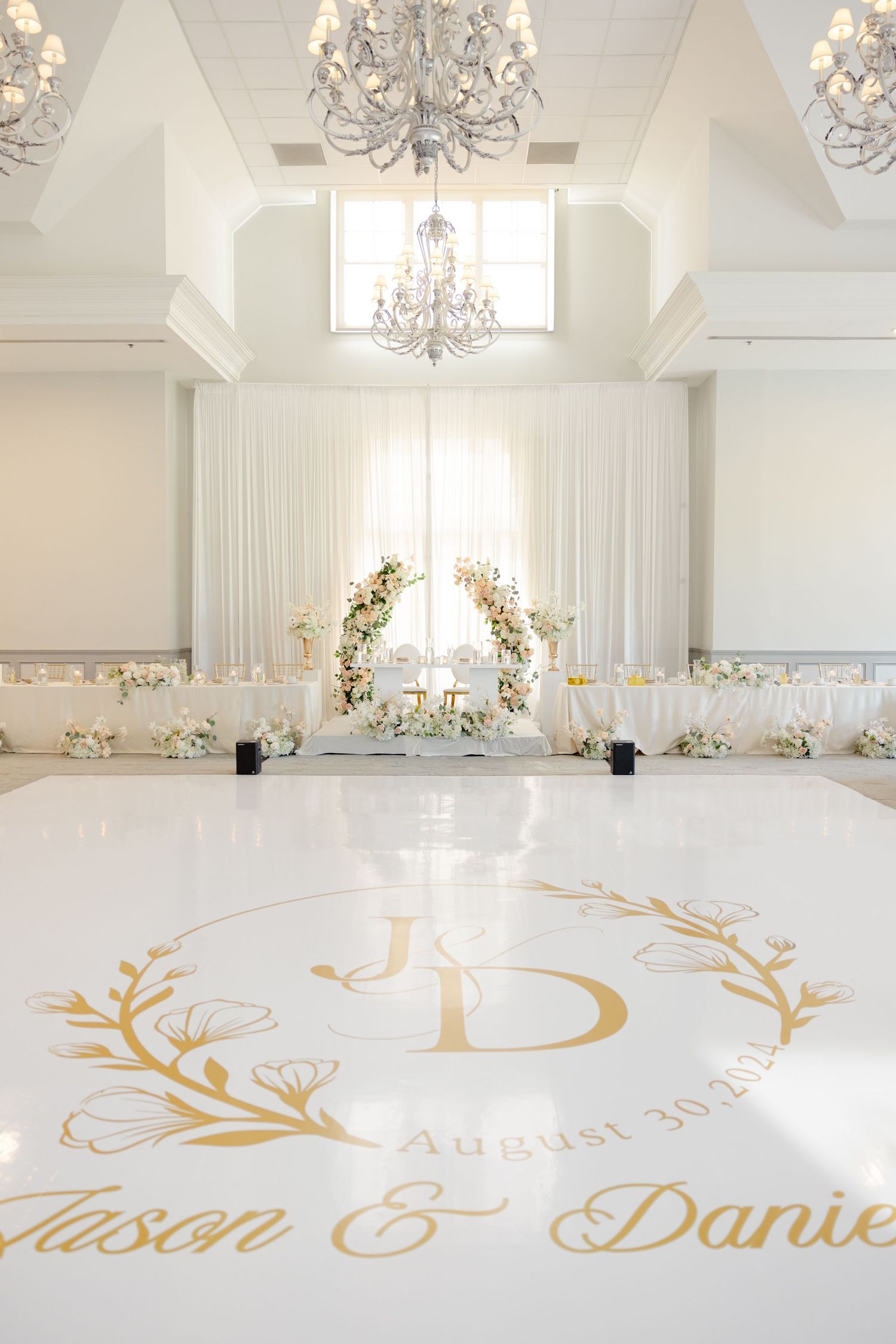 Elegant white ballroom with crystal chandeliers and gold monogram floor decal.