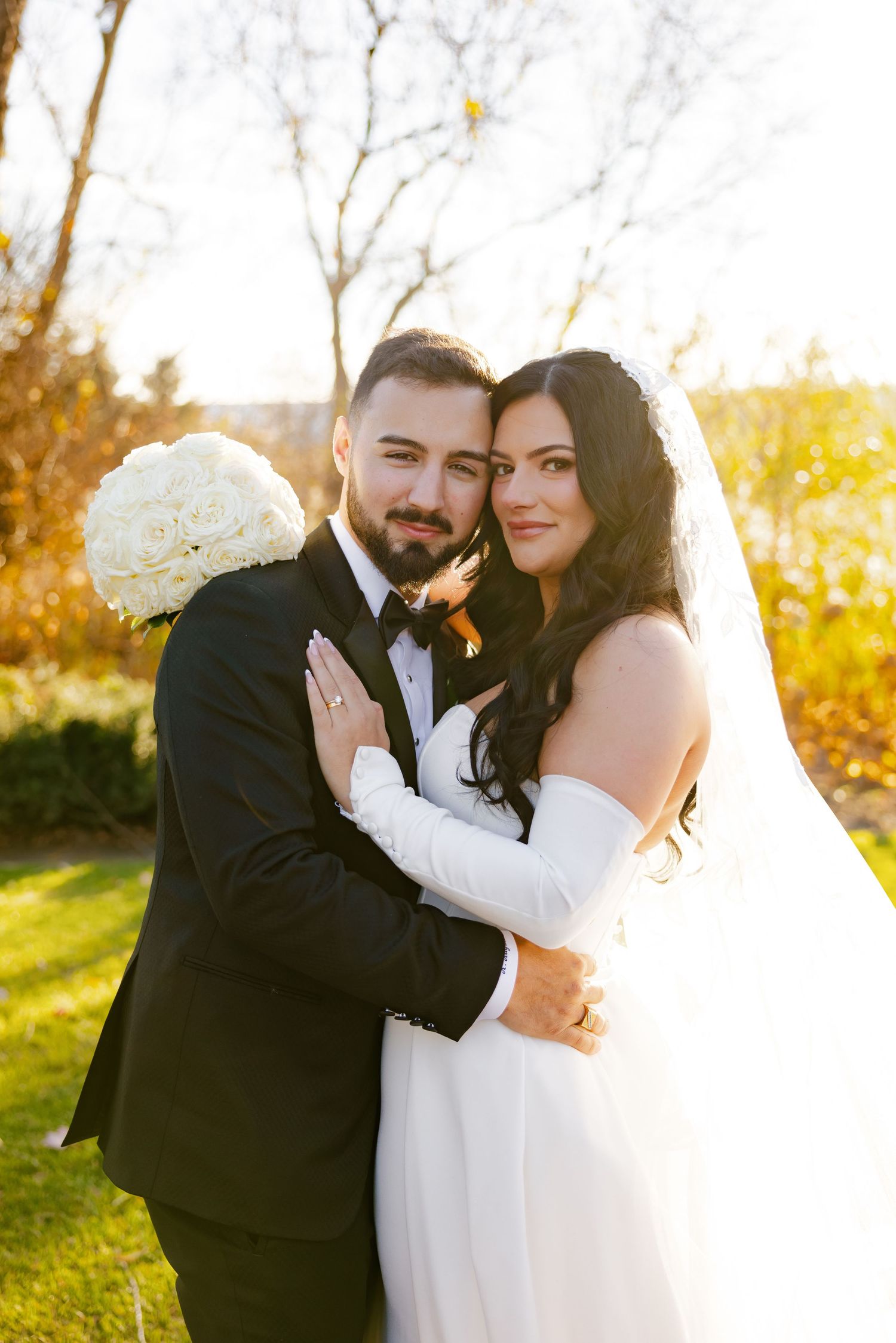Sunlit wedding portrait with bride holding white hydrangea bouquet in autumn garden setting.