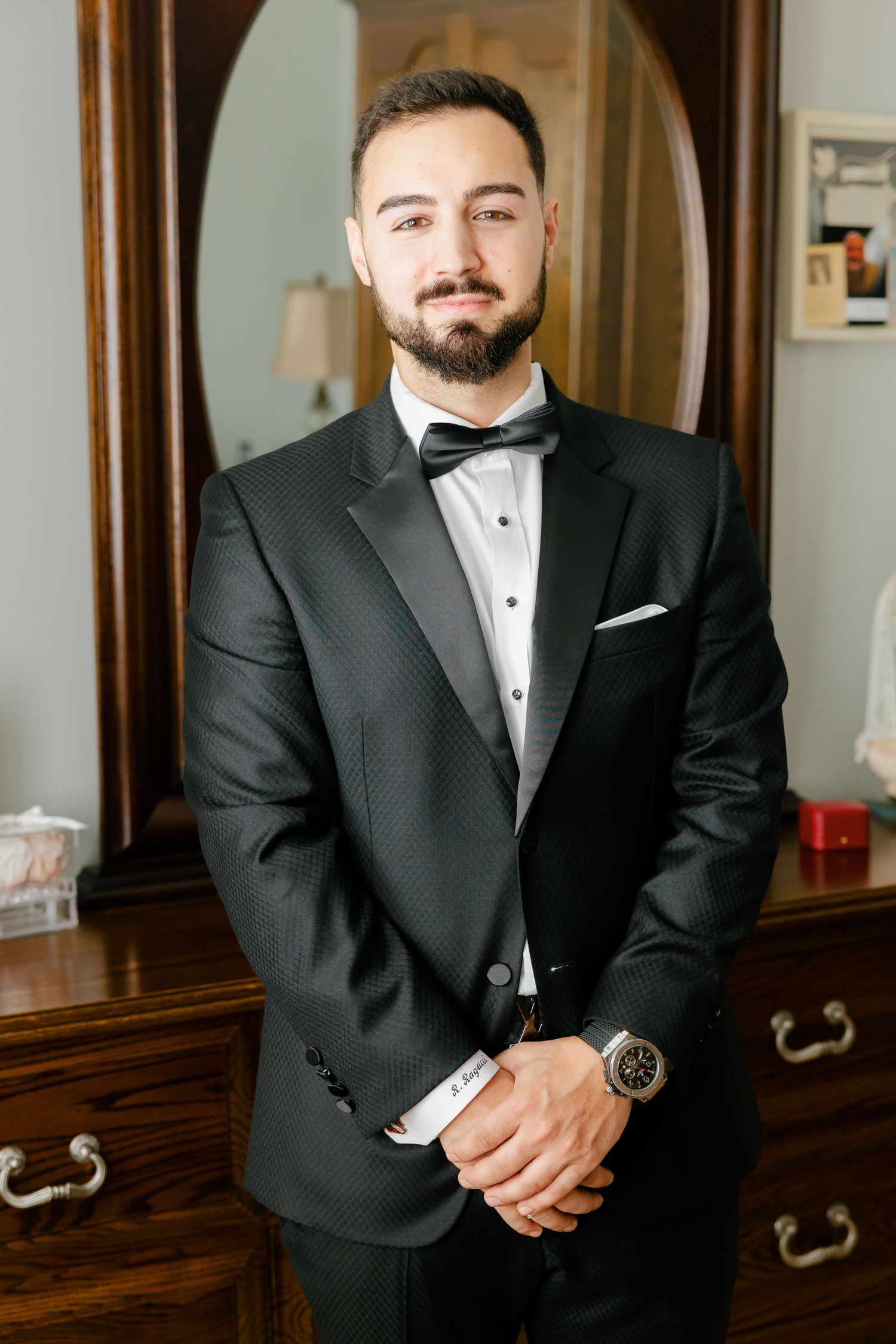 Sharp black tuxedo with satin lapels photographed in front of antique mirror and dresser.
