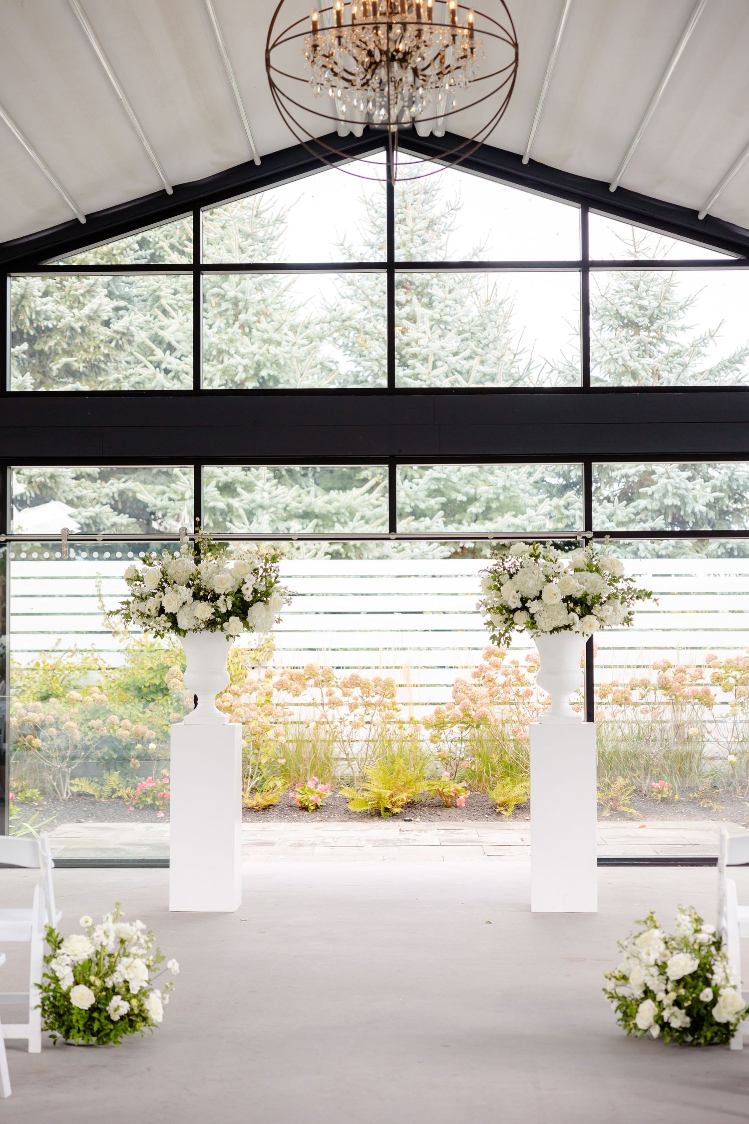 An elegant wedding ceremony space with white floral arrangements on pedestals and a modern chandelier.
