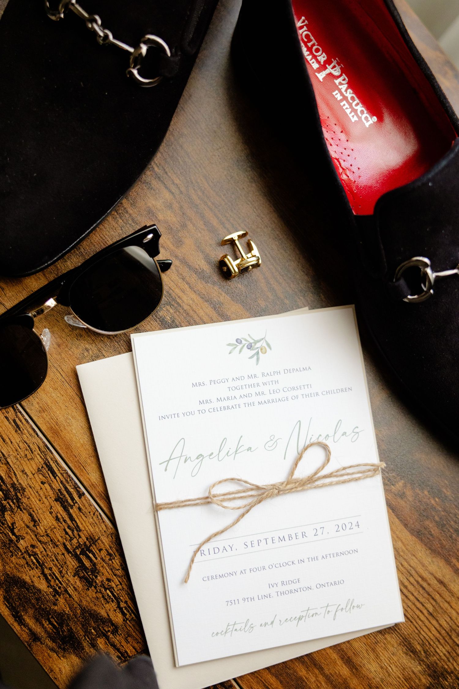 Wedding invitation with twine tied around it next to sunglasses and red bottle.