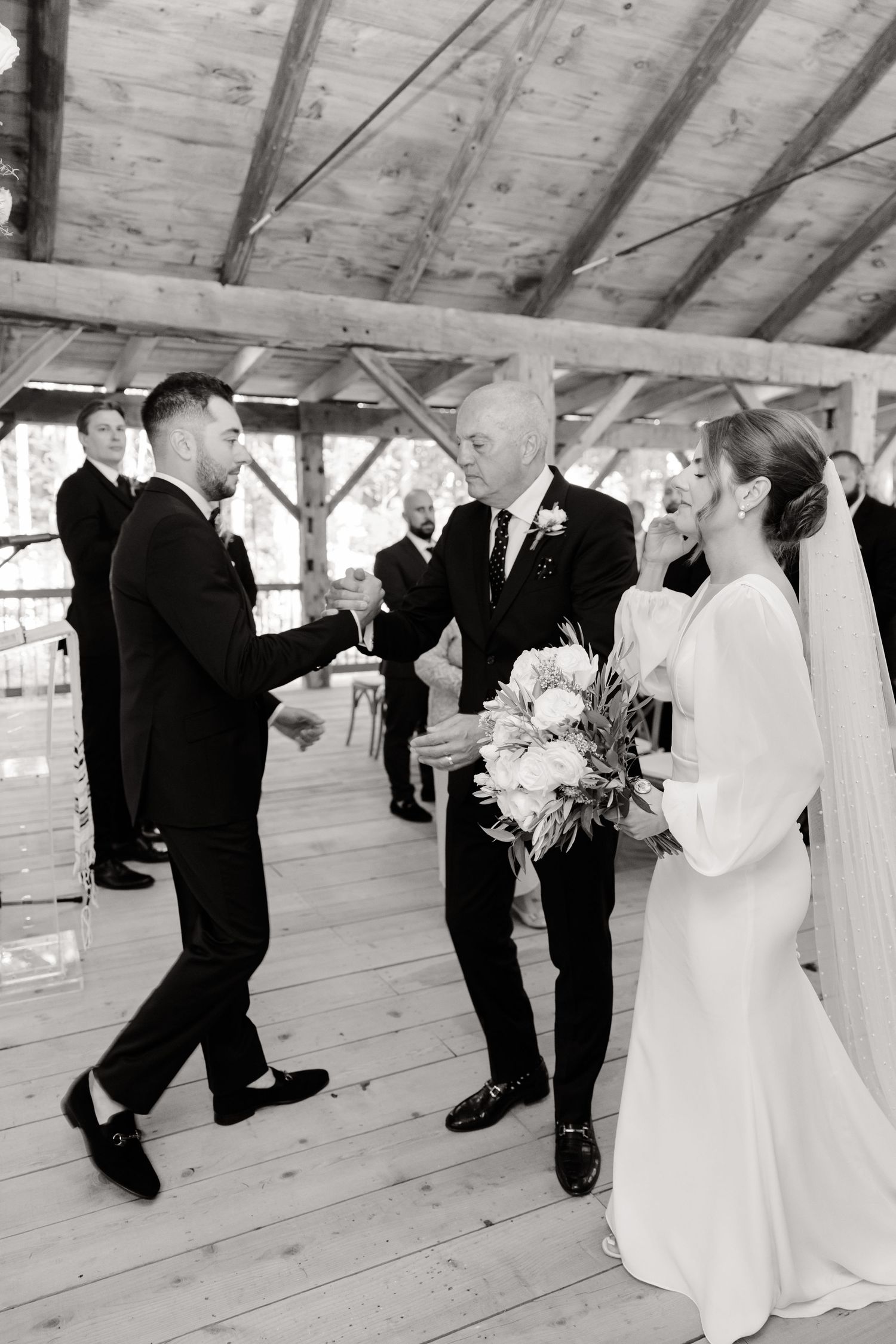 A wedding ceremony moment in a rustic barn with wooden beams and natural lighting.