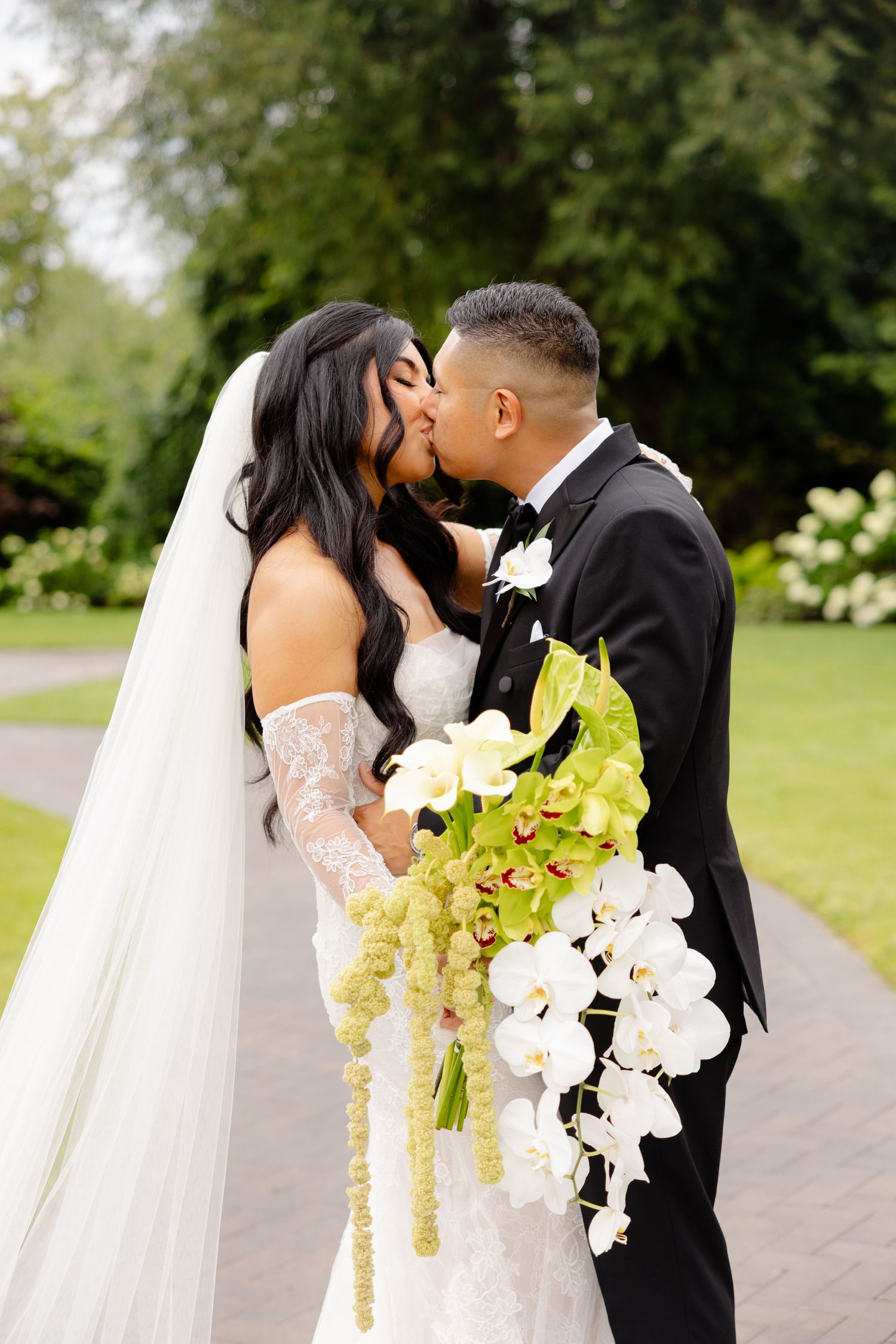 Romantic wedding series of newlywed couple sharing intimate kisses in a garden setting with orchid bouquet.