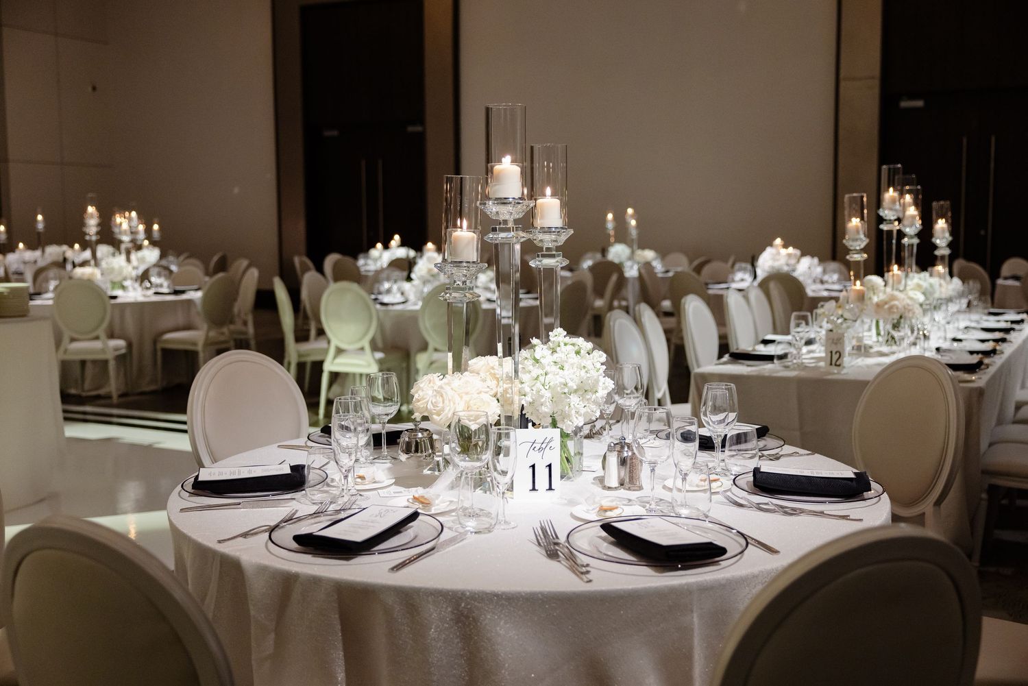 Elegant round dining tables set with white linens and glassware in an upscale banquet hall.