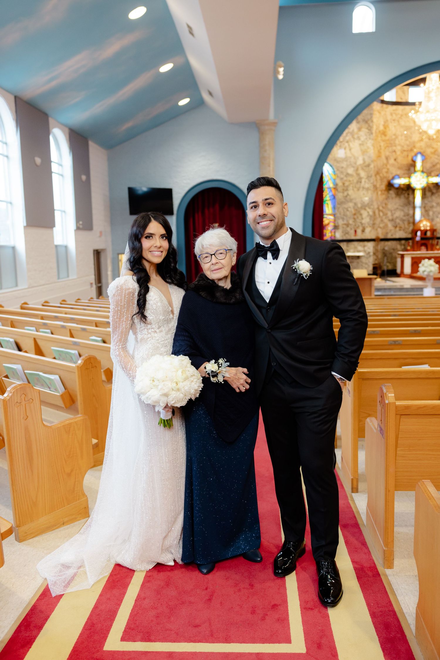Wedding party poses together in church sanctuary with wooden pews and arched architecture.