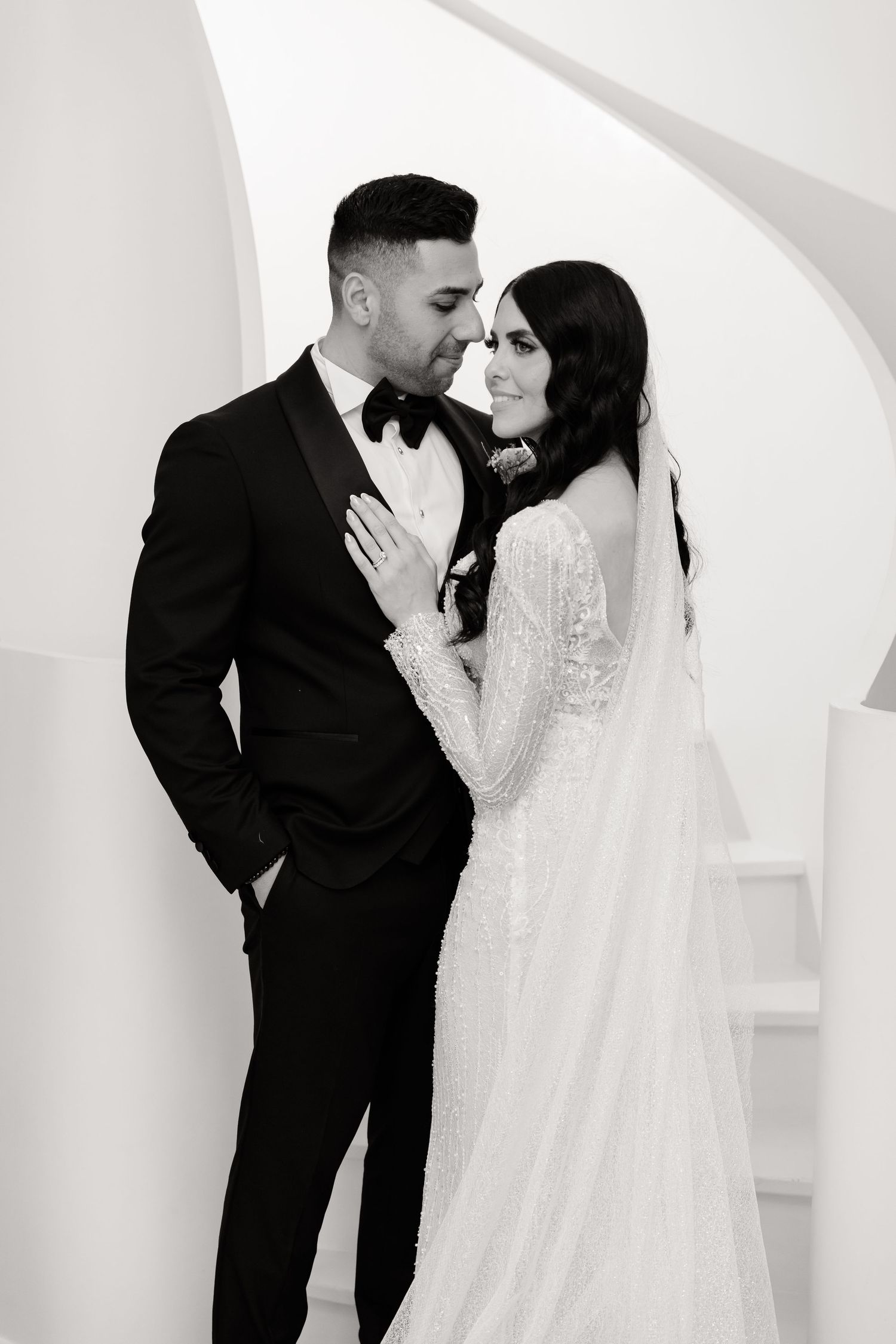 Black and white portrait of a wedding couple in an intimate pose against curved walls.
