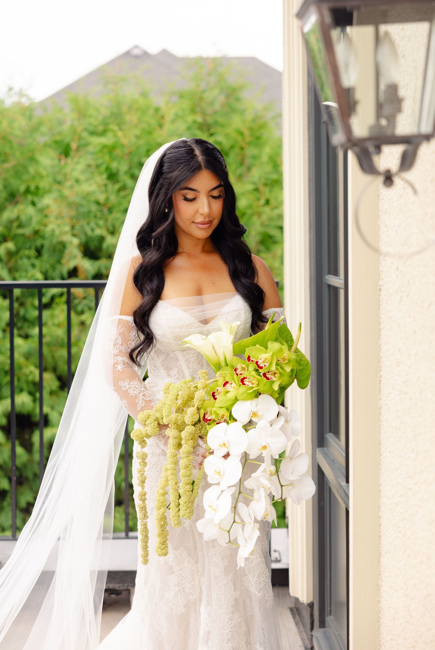 Elegant bride with long dark hair carries stunning cascading bouquet of white orchids and green amaranthus.