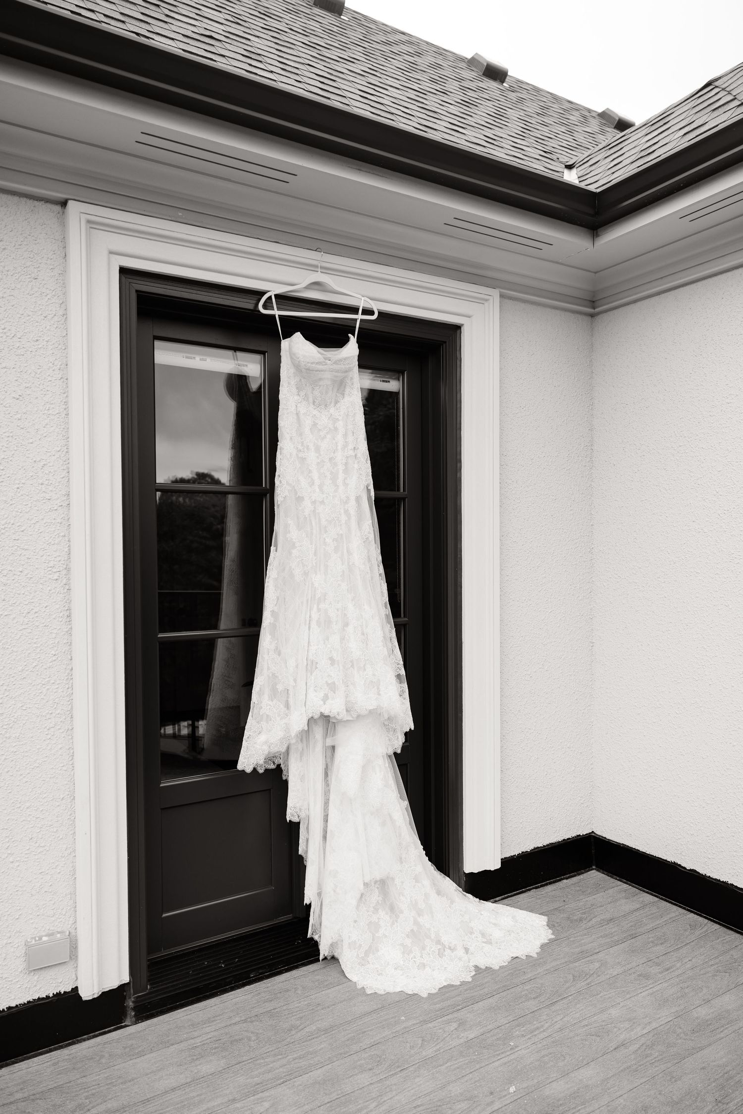 White lace wedding dress hanging in window frames creating a dramatic silhouette against dark background.