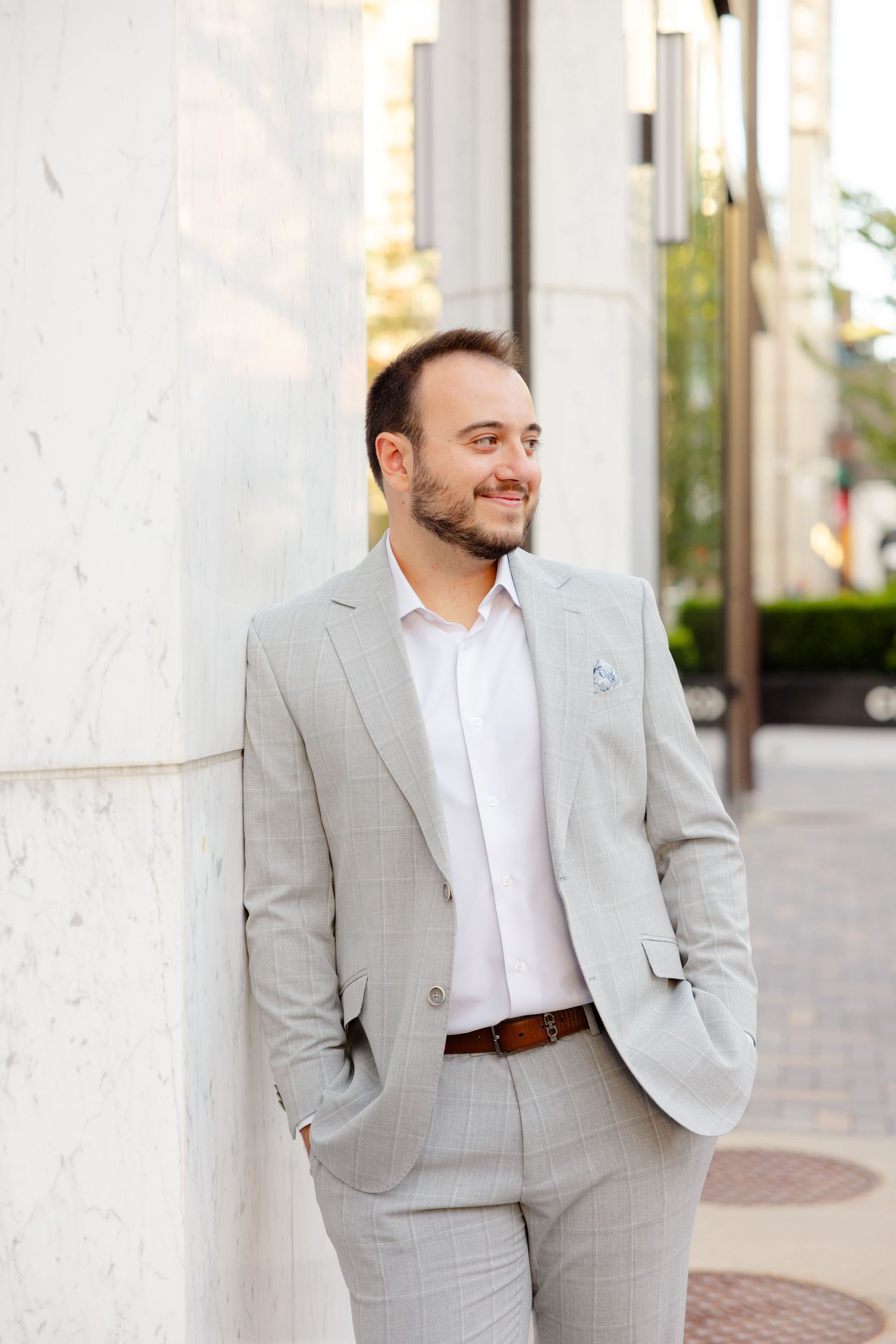Smiling man in business attire poses casually against an urban building exterior.