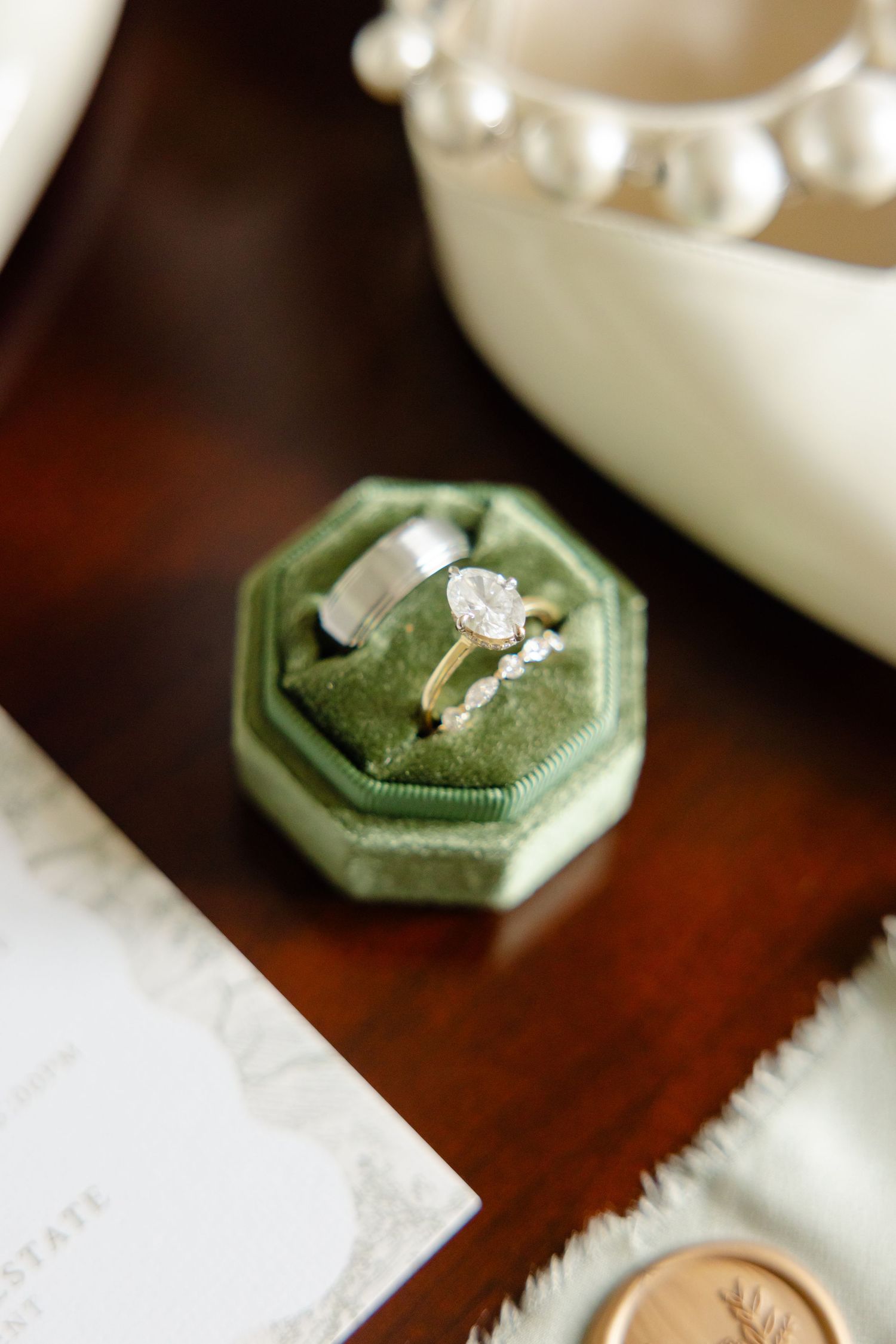 A diamond engagement ring sits in a green velvet ring box on a dark wooden surface.