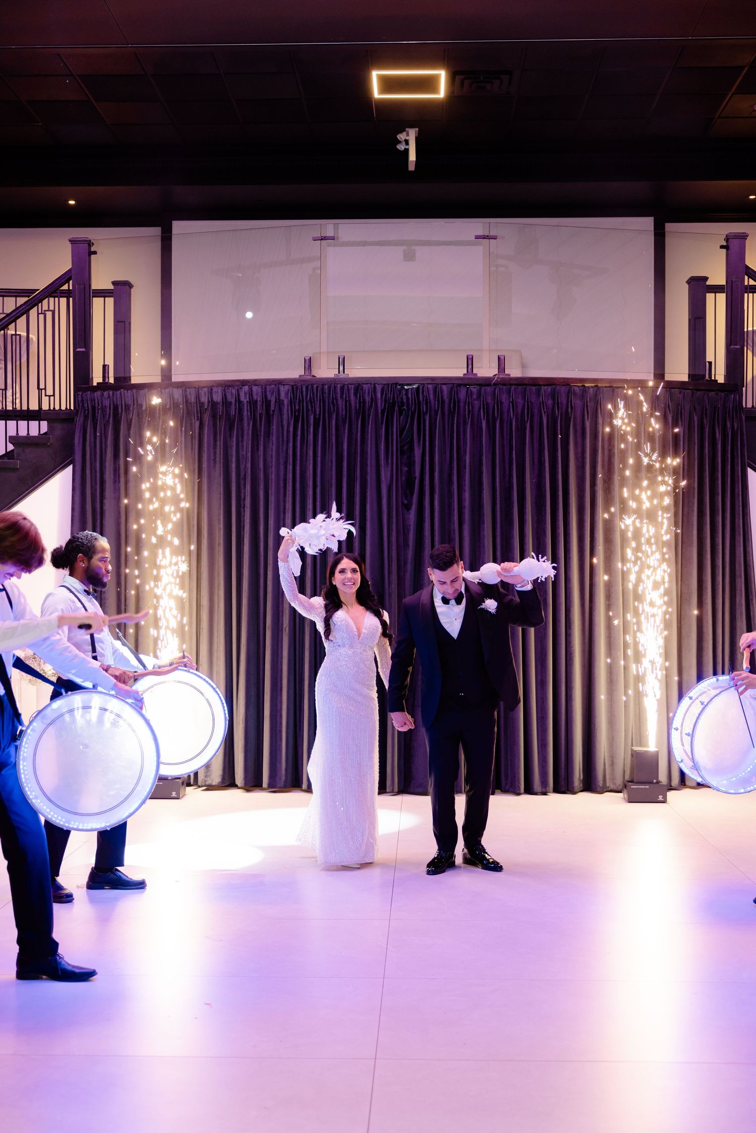 Dramatic wedding ceremony entrance with illuminated columns and traditional drummers creating a grand atmosphere.