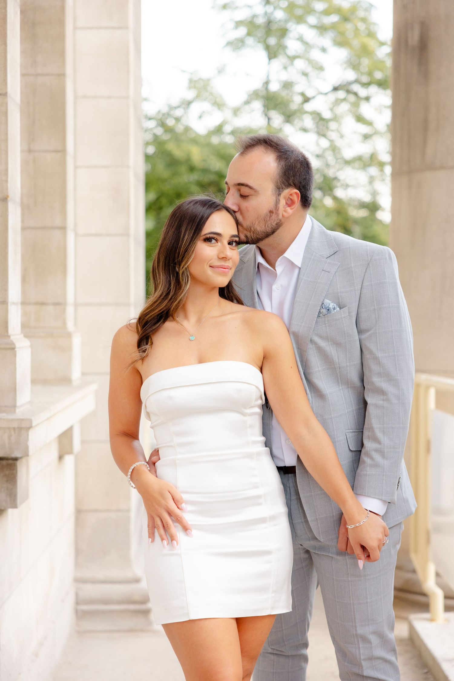 Romantic couple embrace while posing in a classical architectural setting.