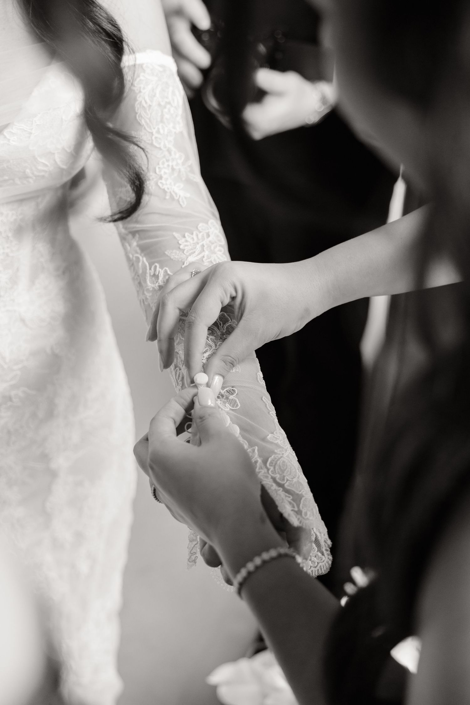 A delicate moment captured in black and white as someone adjusts the lace sleeve of an elegant wedding dress.
