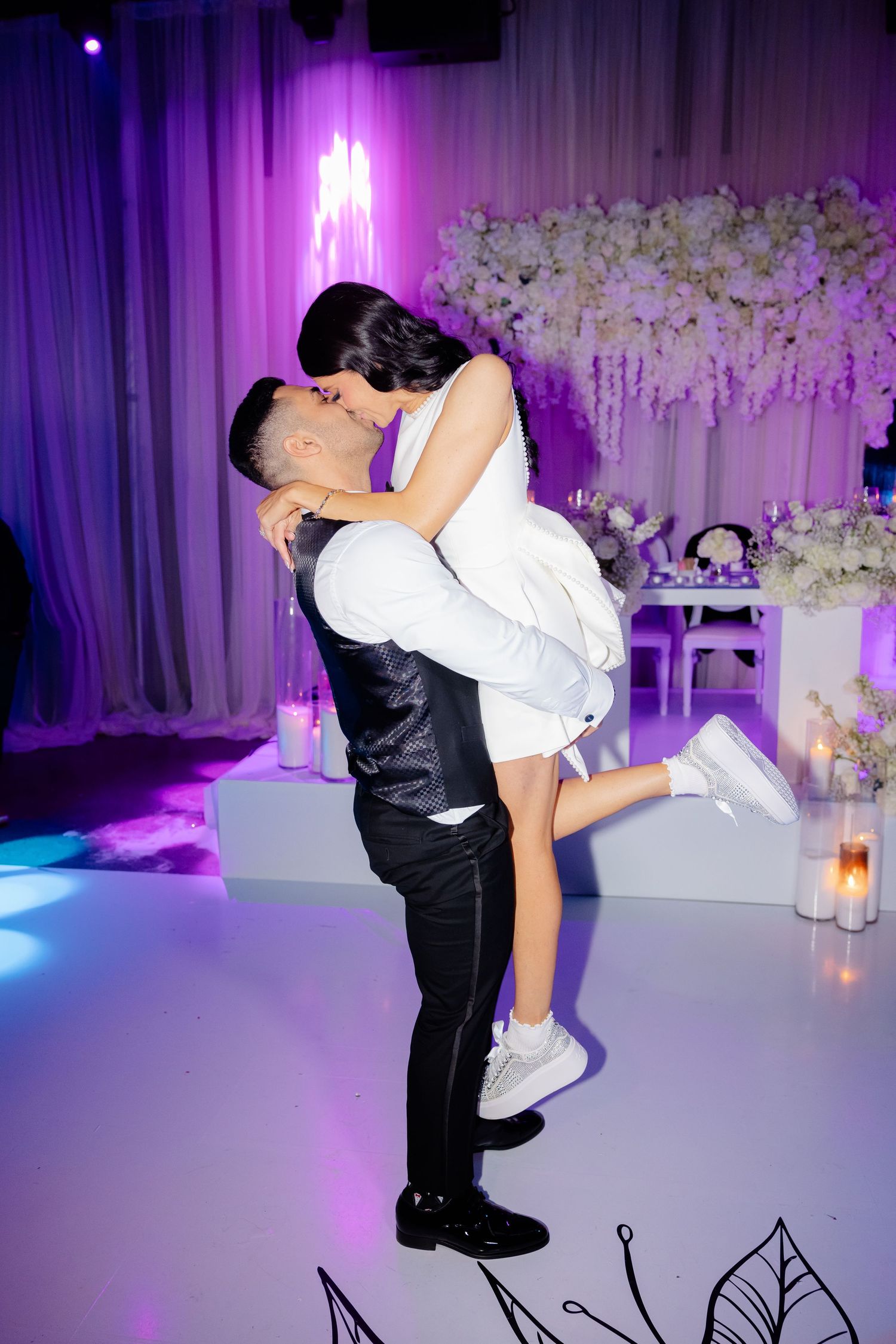 Romantic dance lift pose at elegant wedding reception with purple ambient lighting.