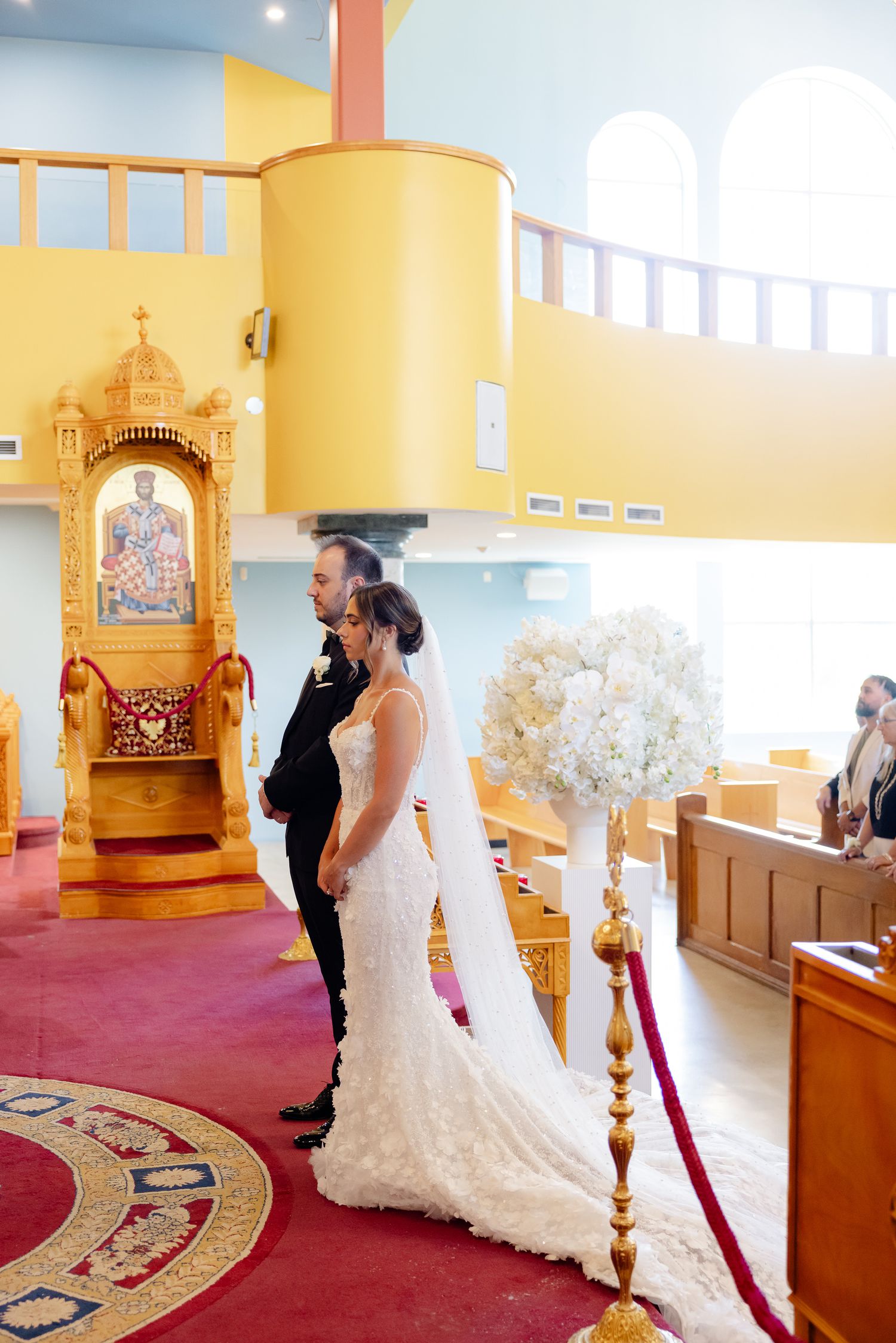 A couple shares a special moment inside a church during their wedding ceremony with yellow walls and red carpet.