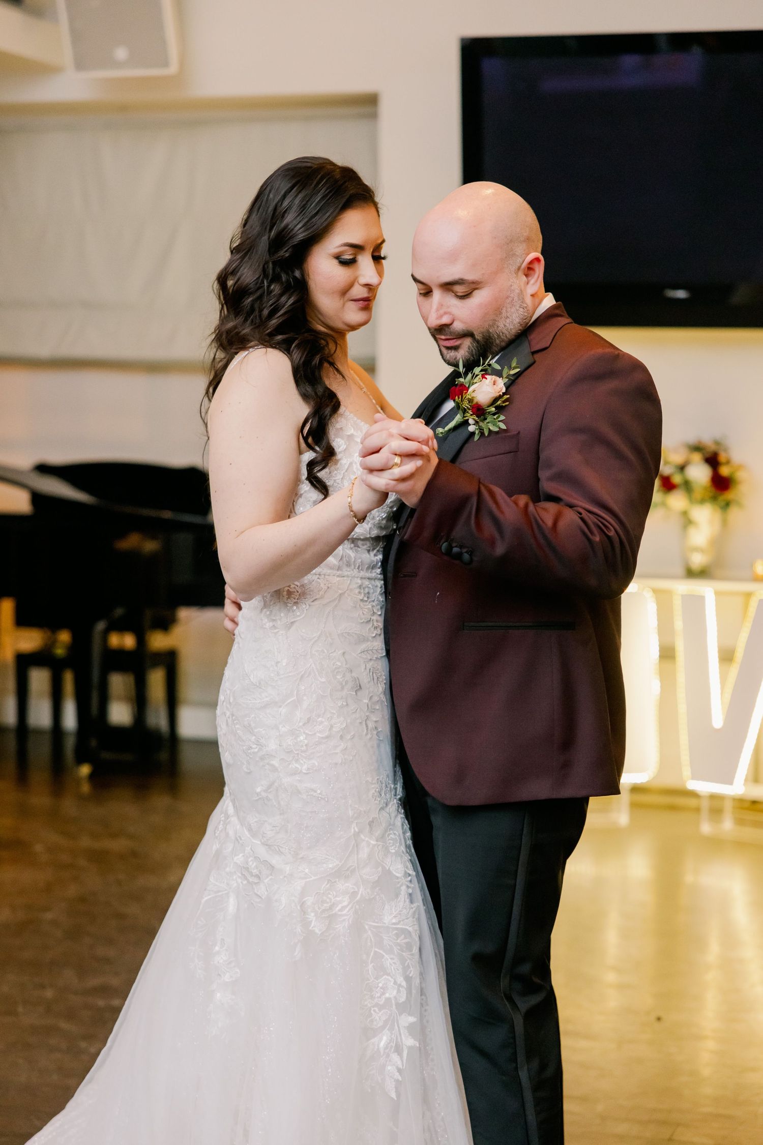 First dance at wedding reception with couple in burgundy suit and lace gown.