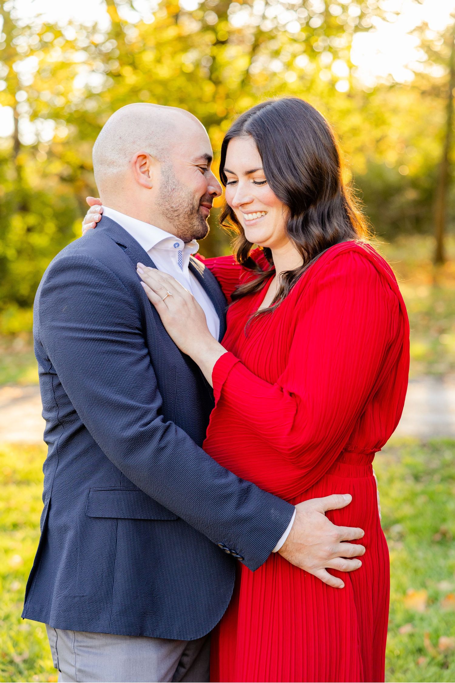 Intimate moment between couple in navy suit and red dress during autumn photoshoot.