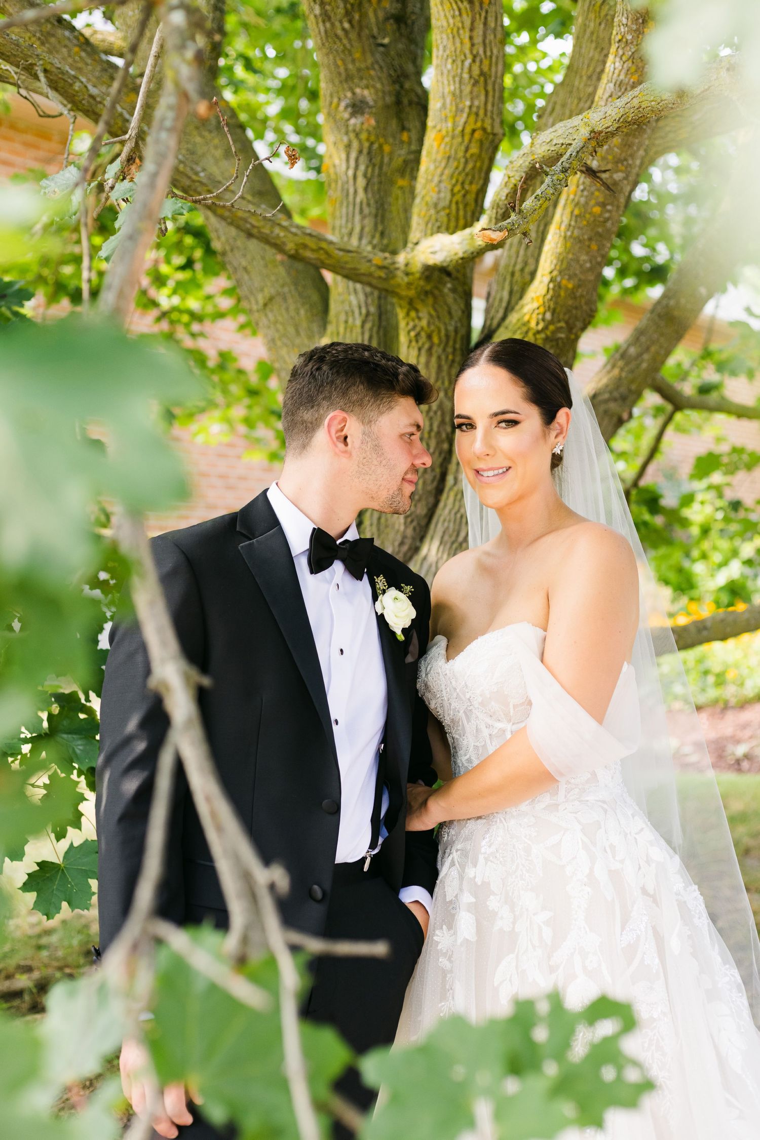 Elegant wedding portrait captured through green foliage with natural lighting.