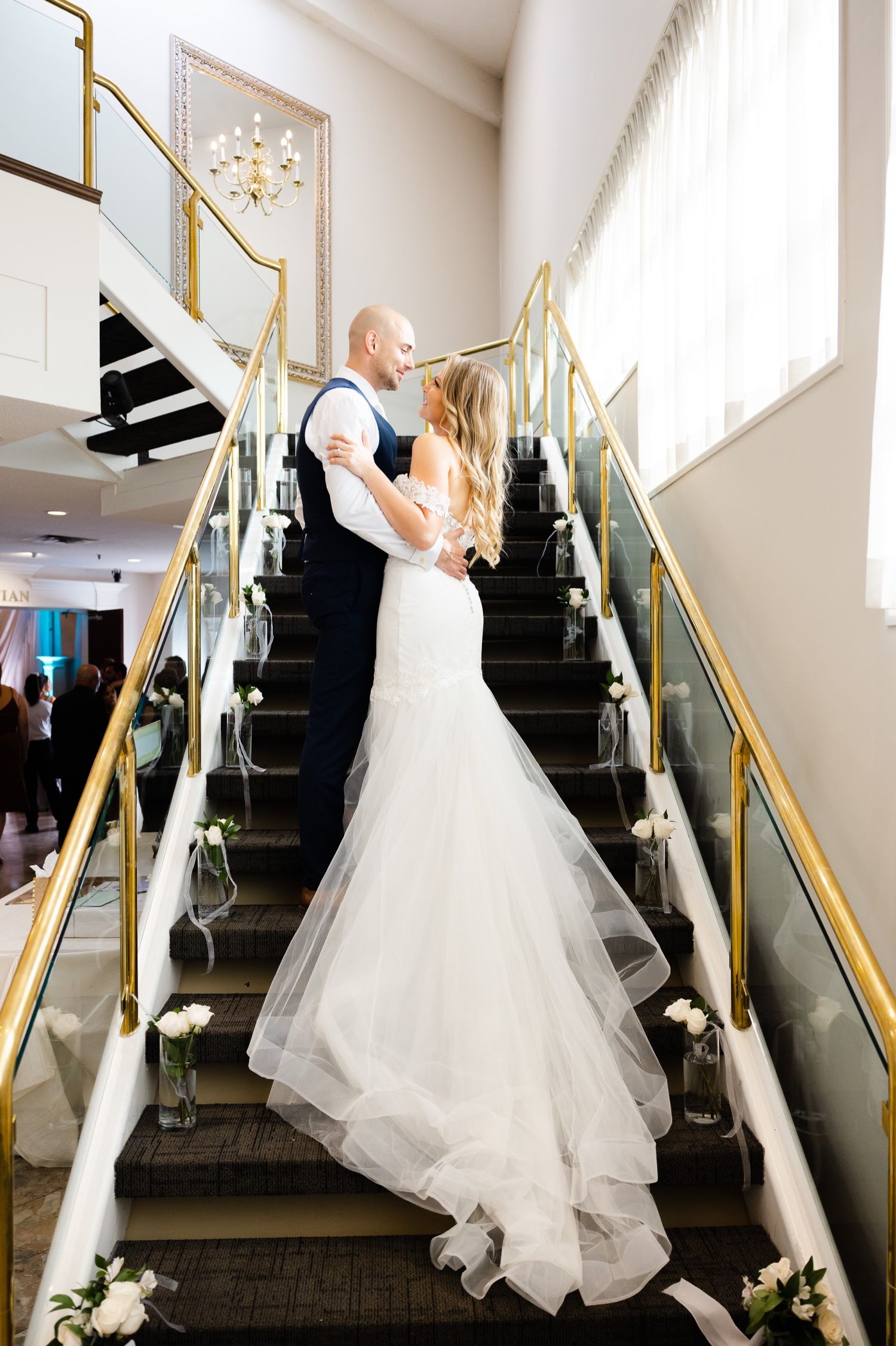 Elegant wedding portrait on a staircase with gold railings and white floral decorations.