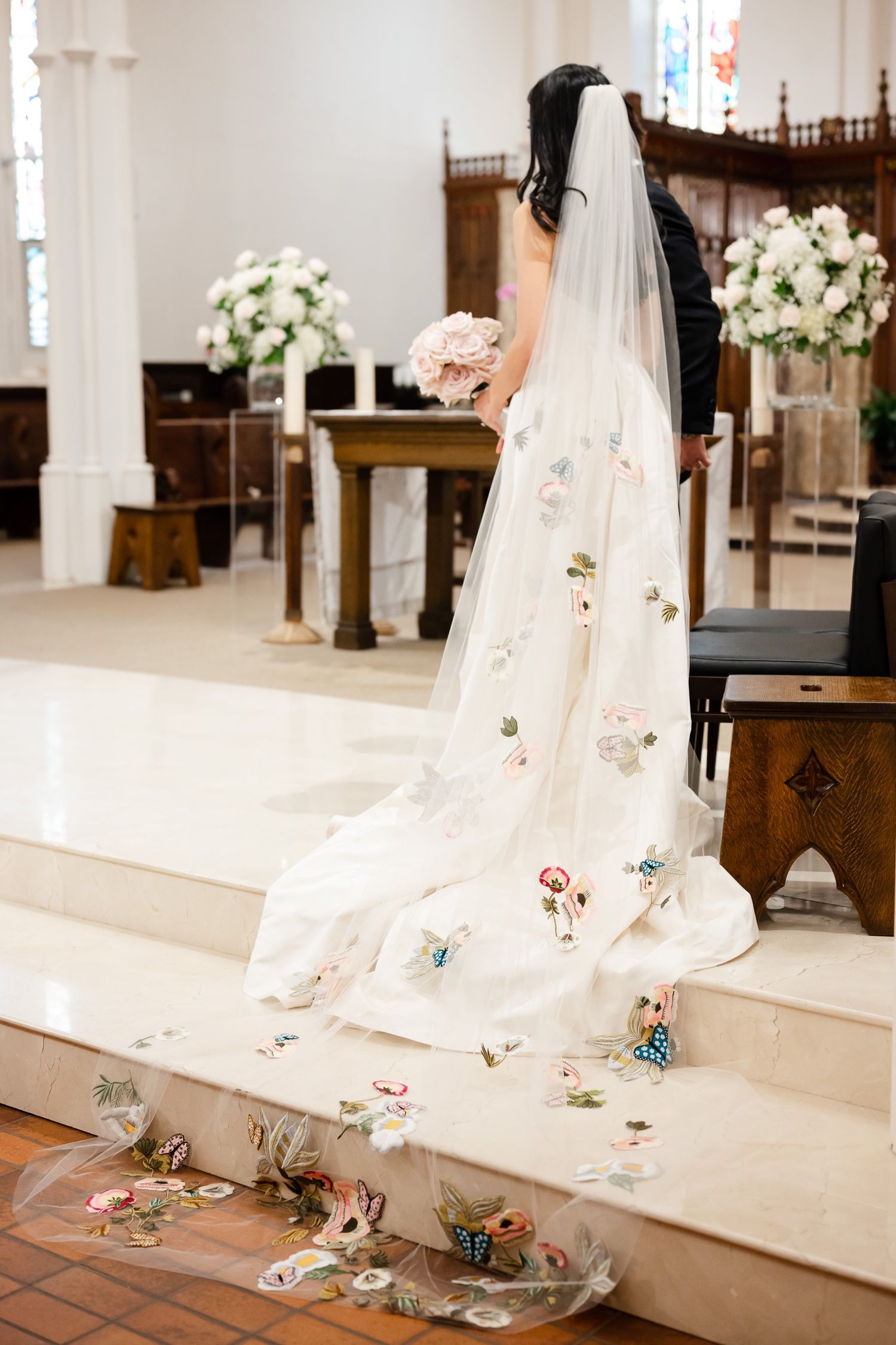 A long white wedding veil with delicate floral embellishments trailing down church steps in a cathedral setting.
