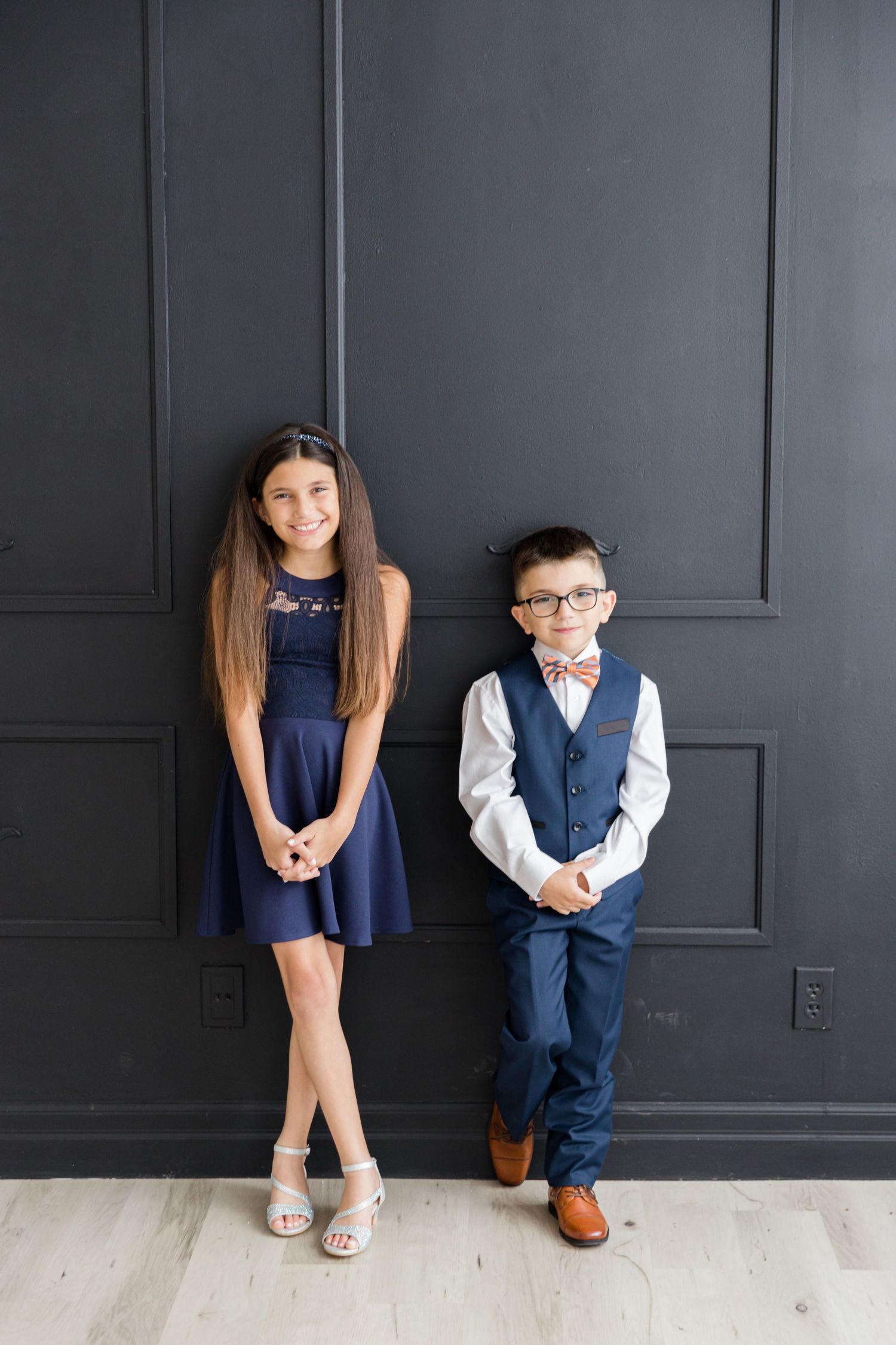 Coordinated navy formal wear portrait against dark wall with light wooden flooring.