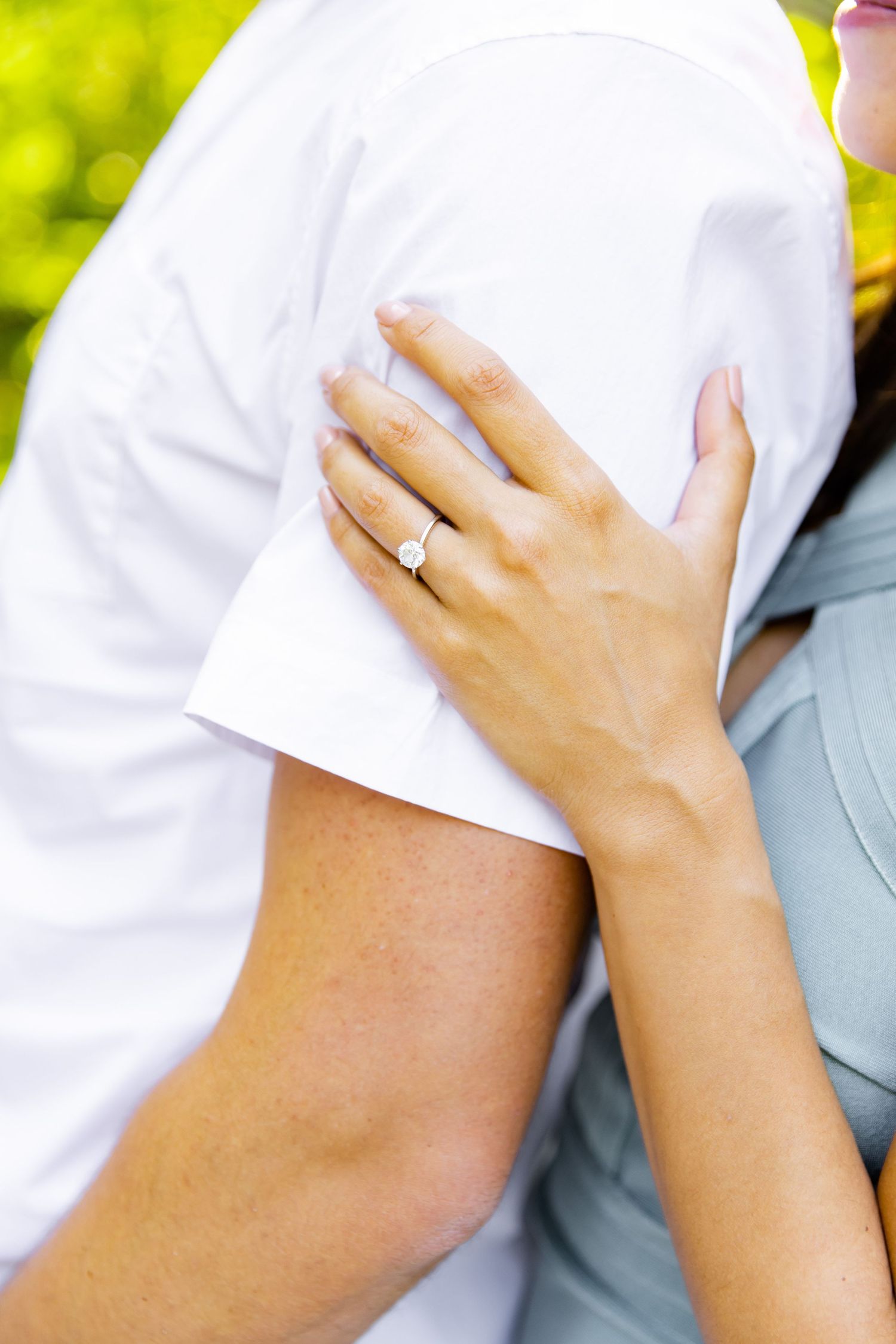 Close up of hands showing an engagement ring against a white shirt sleeve.