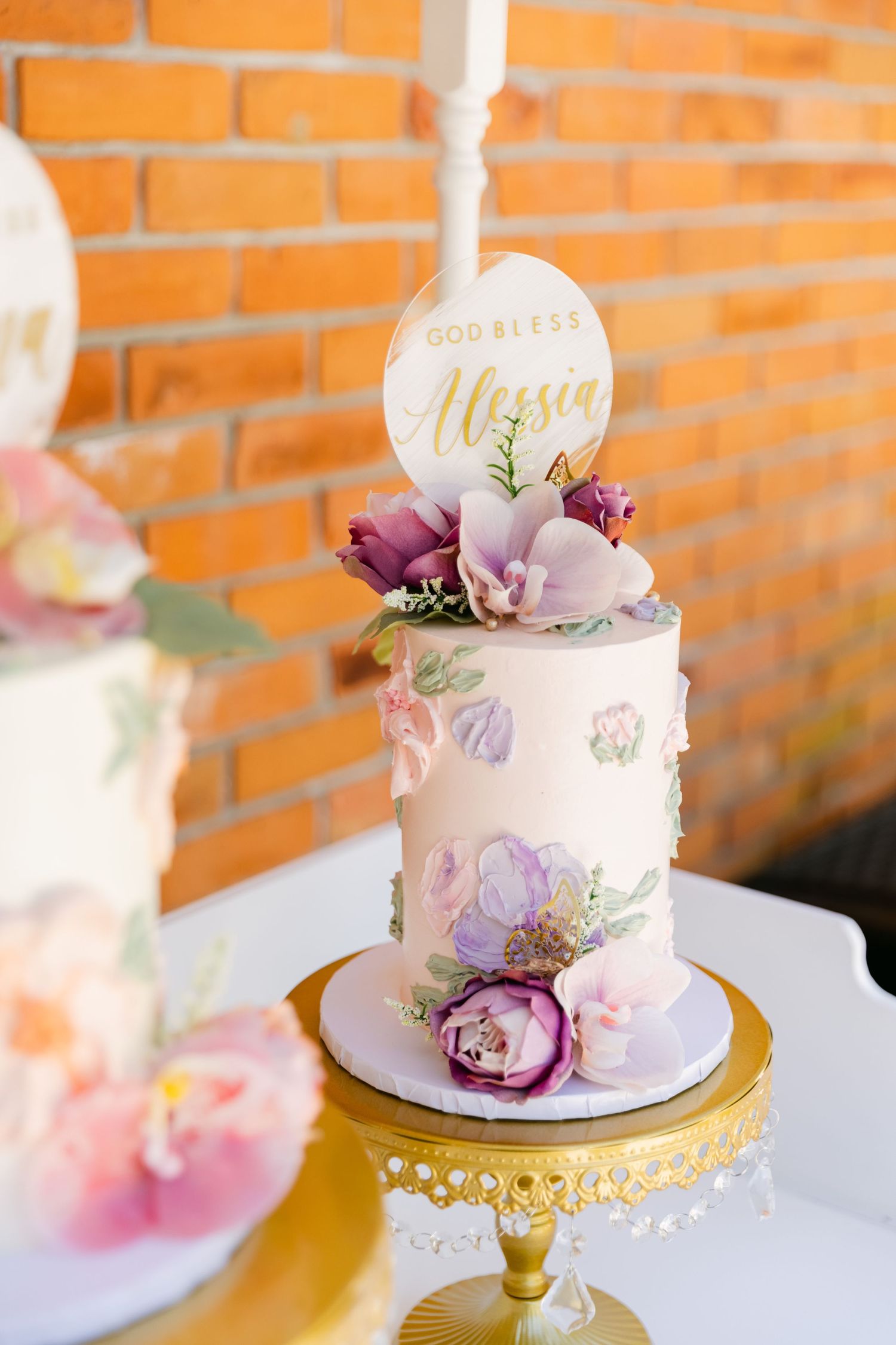 Romantic wedding cake decorated with purple and pink flowers and gold accents on an ornate gold stand.