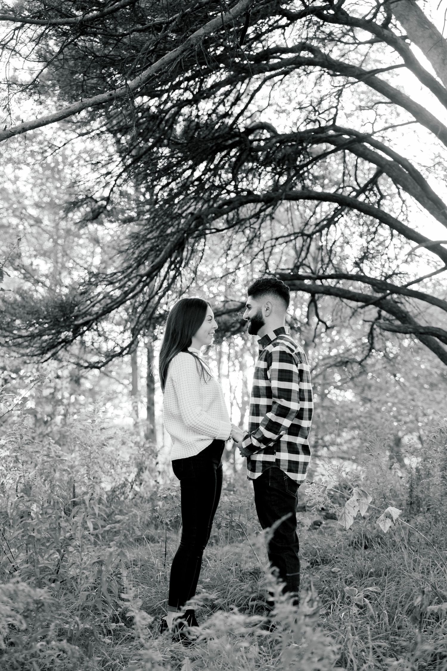Black and white portrait of couple standing beneath sprawling tree branches.