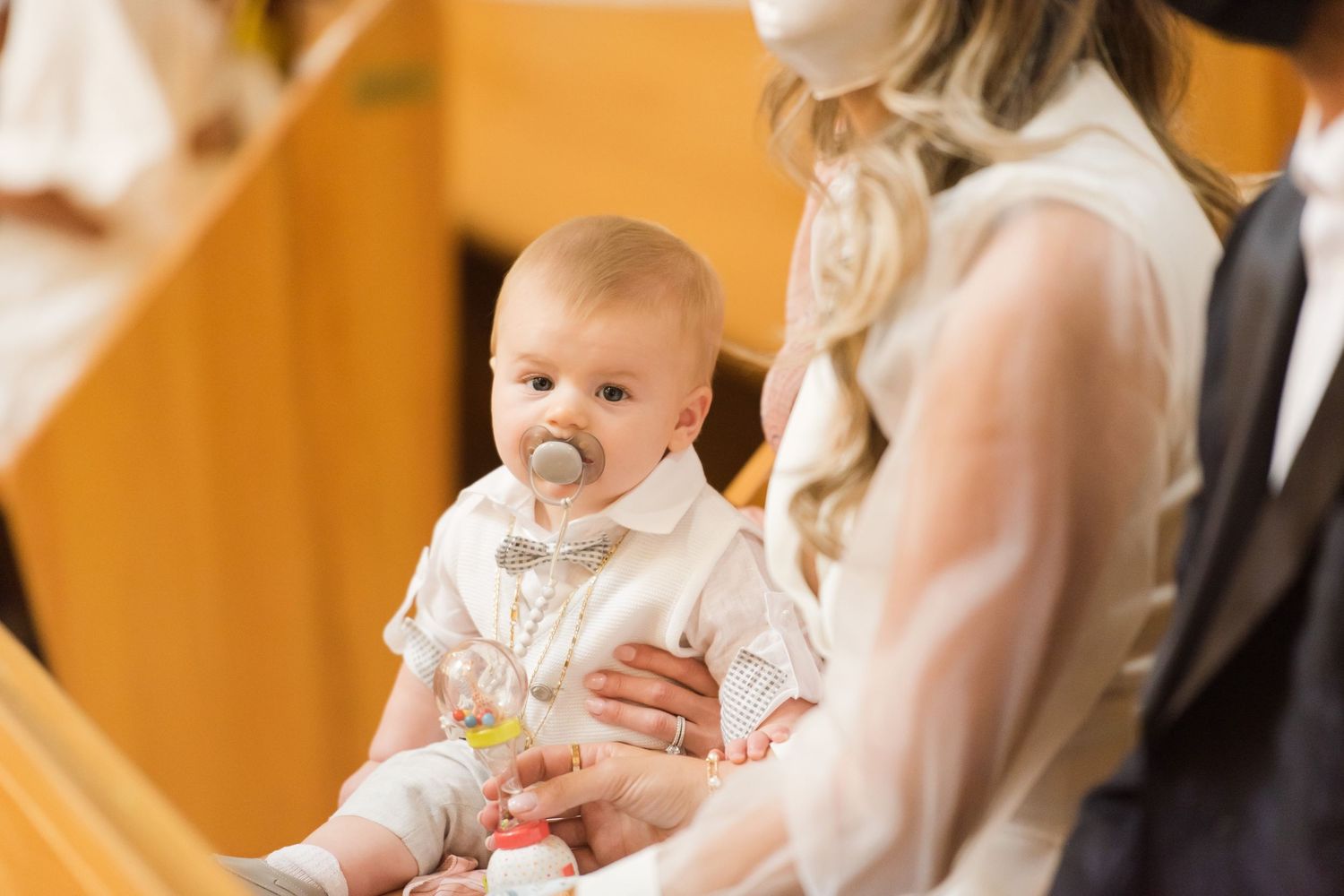 Baby in white baptismal gown being held during religious ceremony in church.