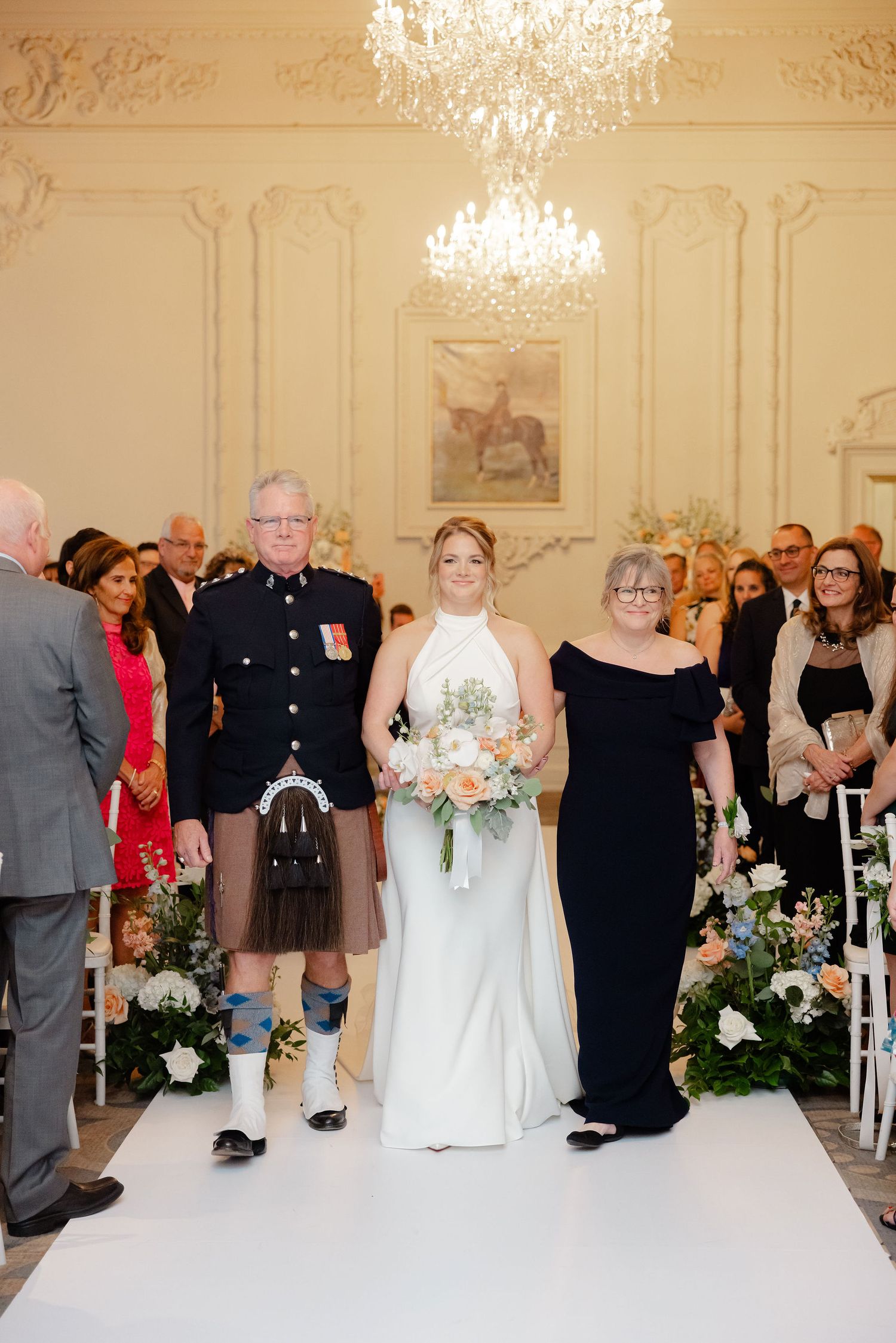 Wedding party members walking down the aisle in formal attire during an elegant indoor ceremony.