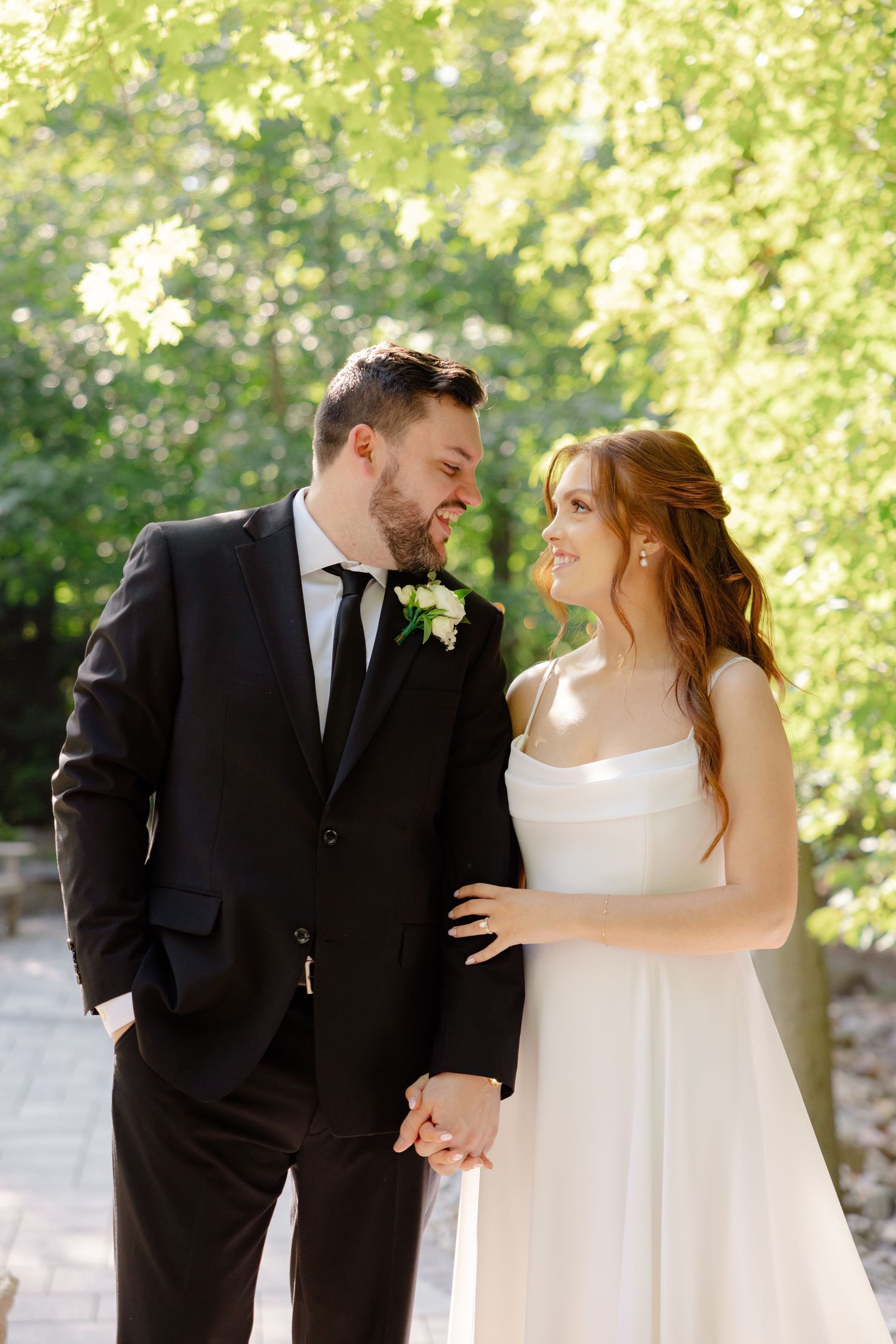 A sunlit wedding portrait showing a couple in classic black and white attire on a garden path.