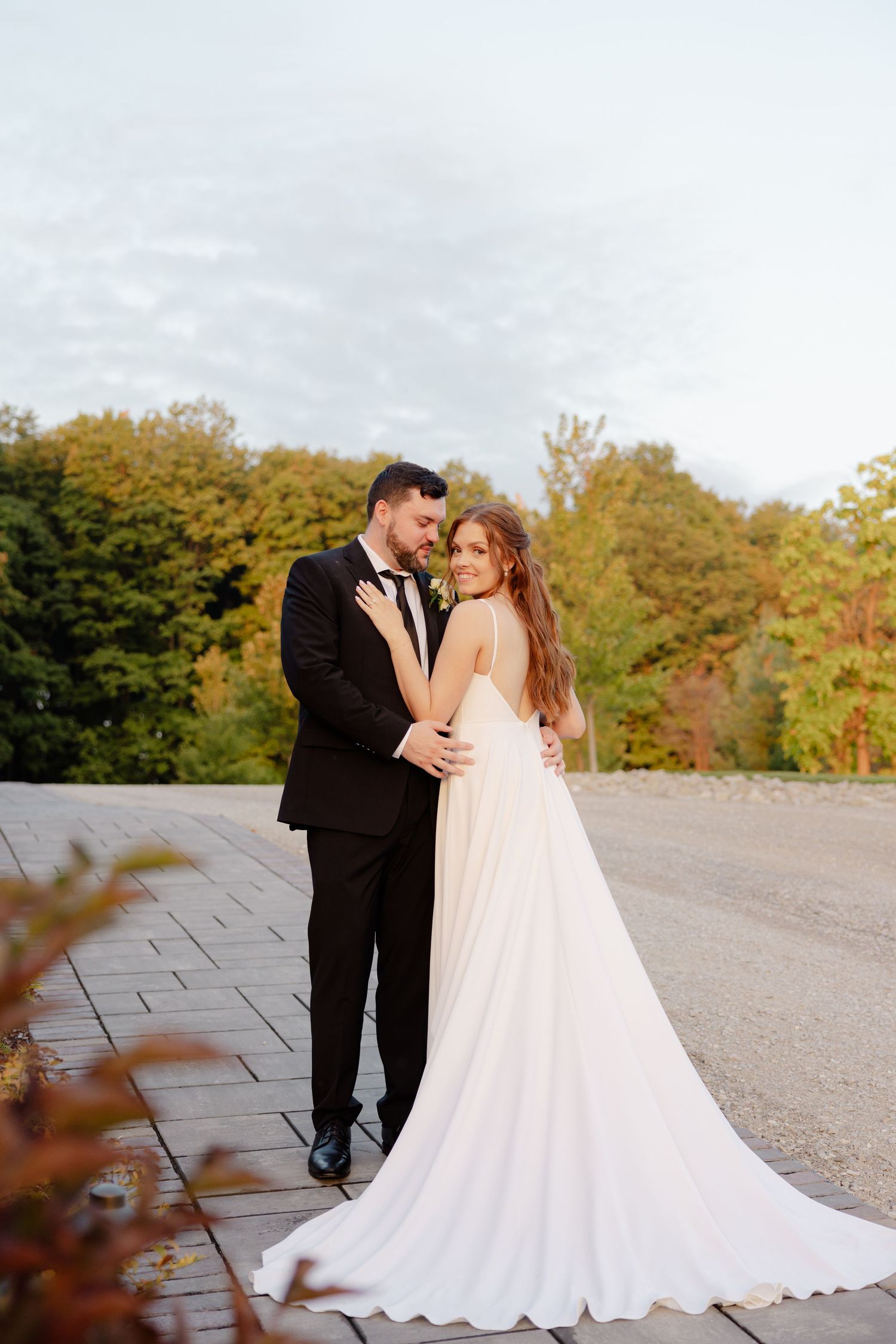 Wedding couple enjoys a tender embrace on stone pavement with autumn colors in the background.