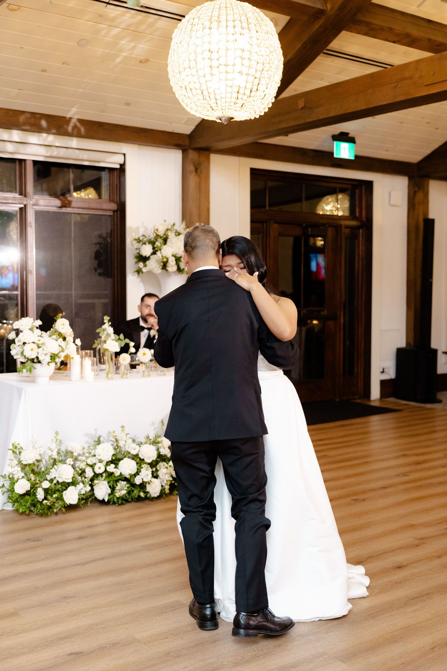 First dance in an elegant reception hall with crystal chandelier and floral decorations.