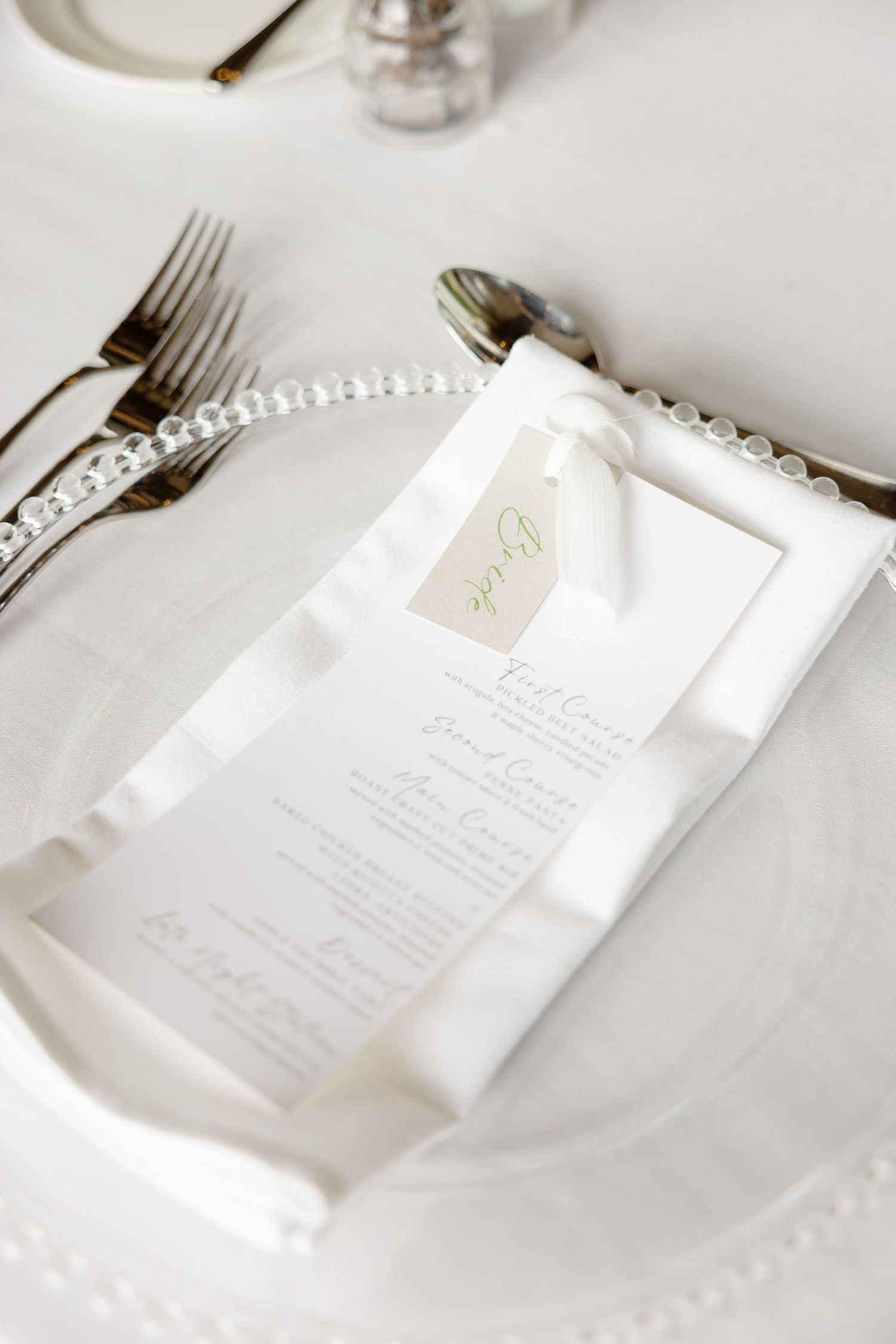 Wedding menu card with pearl trim placed on white china plate with elegant silverware.