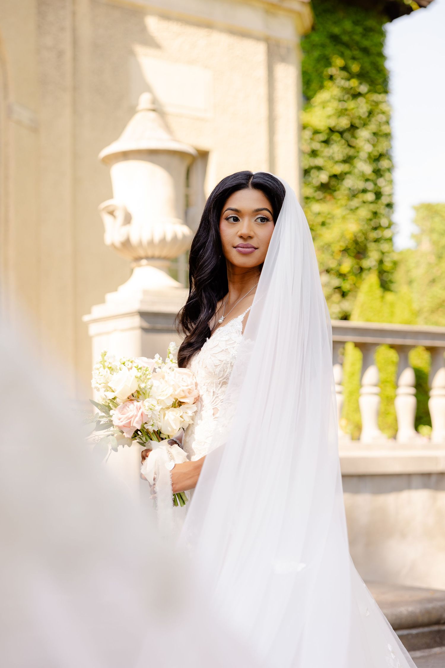 A bride holds a blush bouquet while posing in front of a grand historic building with ornate architecture.