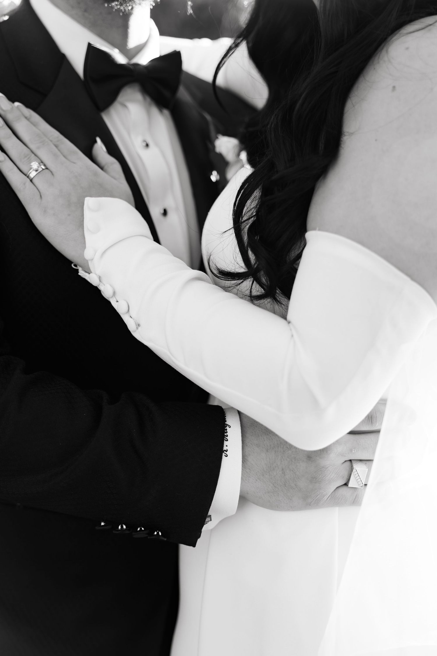 Close-up black and white detail shot of bride and groom's embrace showing wedding attire.