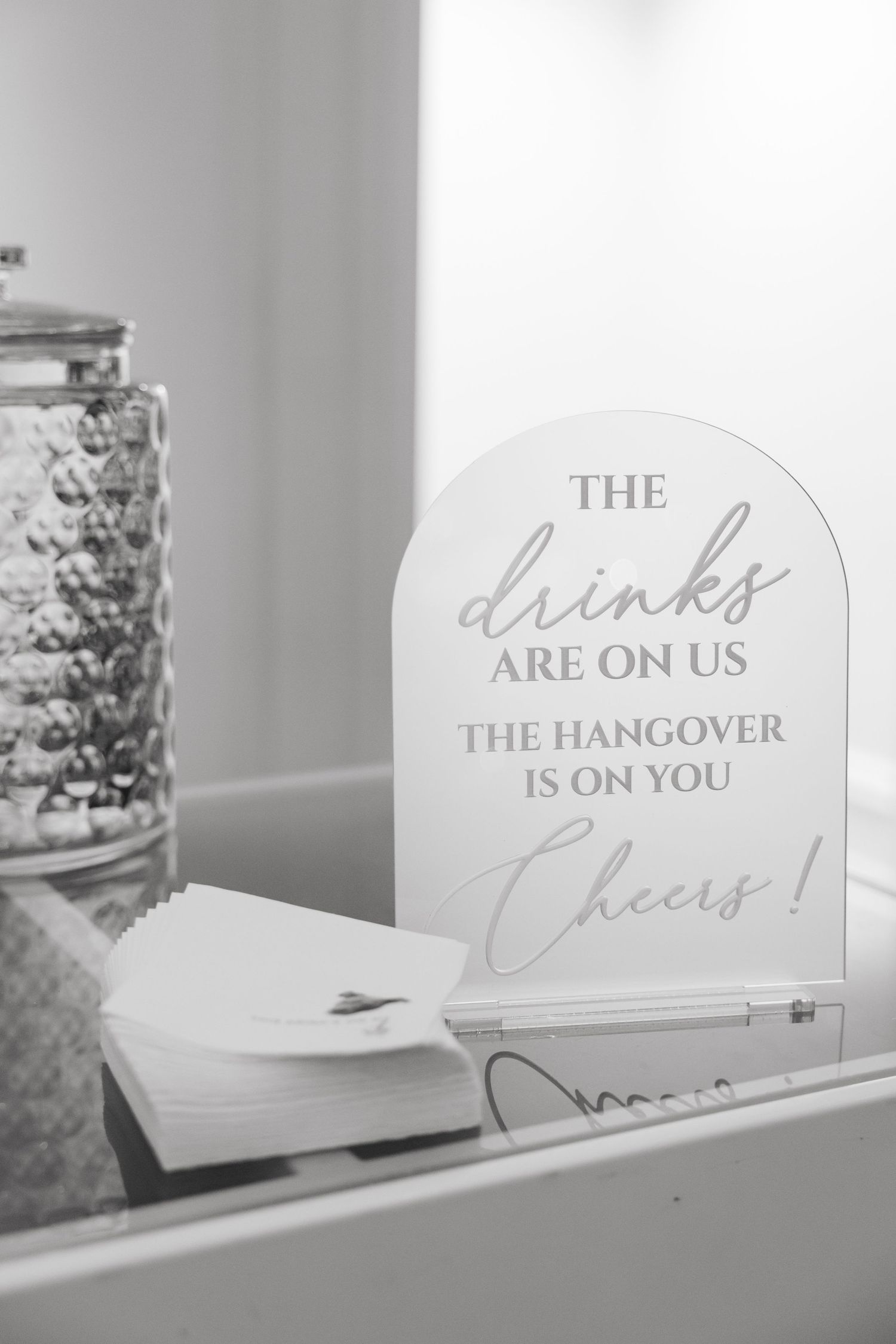 A decorative sign reading 'The drinks are on us, the hangover is on you' displayed next to a glass container.