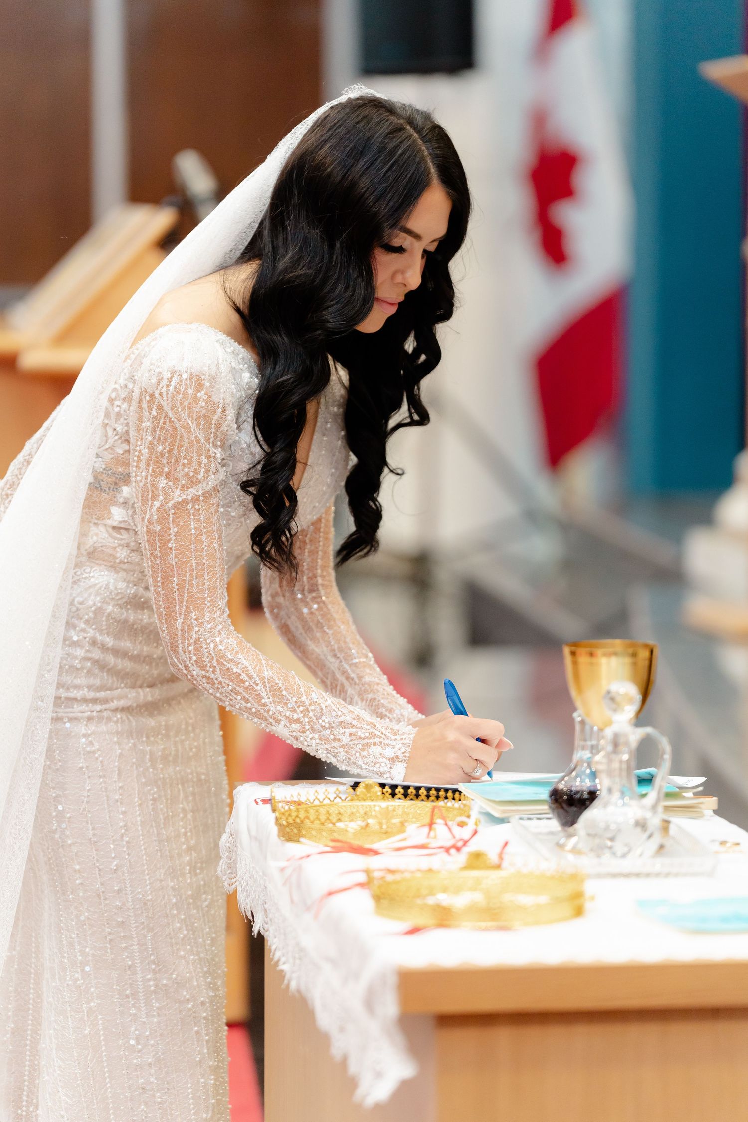 Bride in lace gown signs wedding documents at decorated altar table.